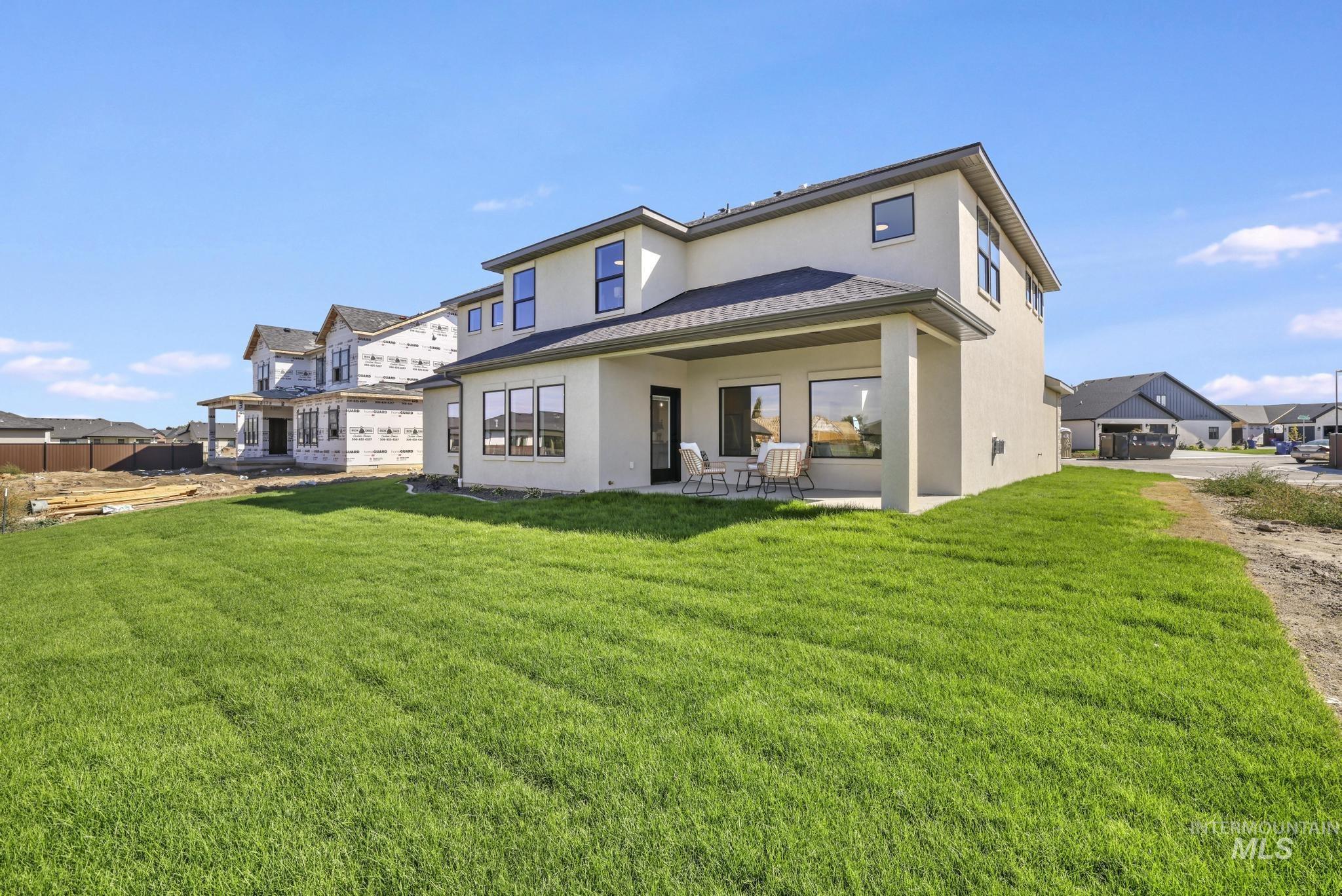 Rear view of house with stucco siding, a patio area, a yard, and a residential view