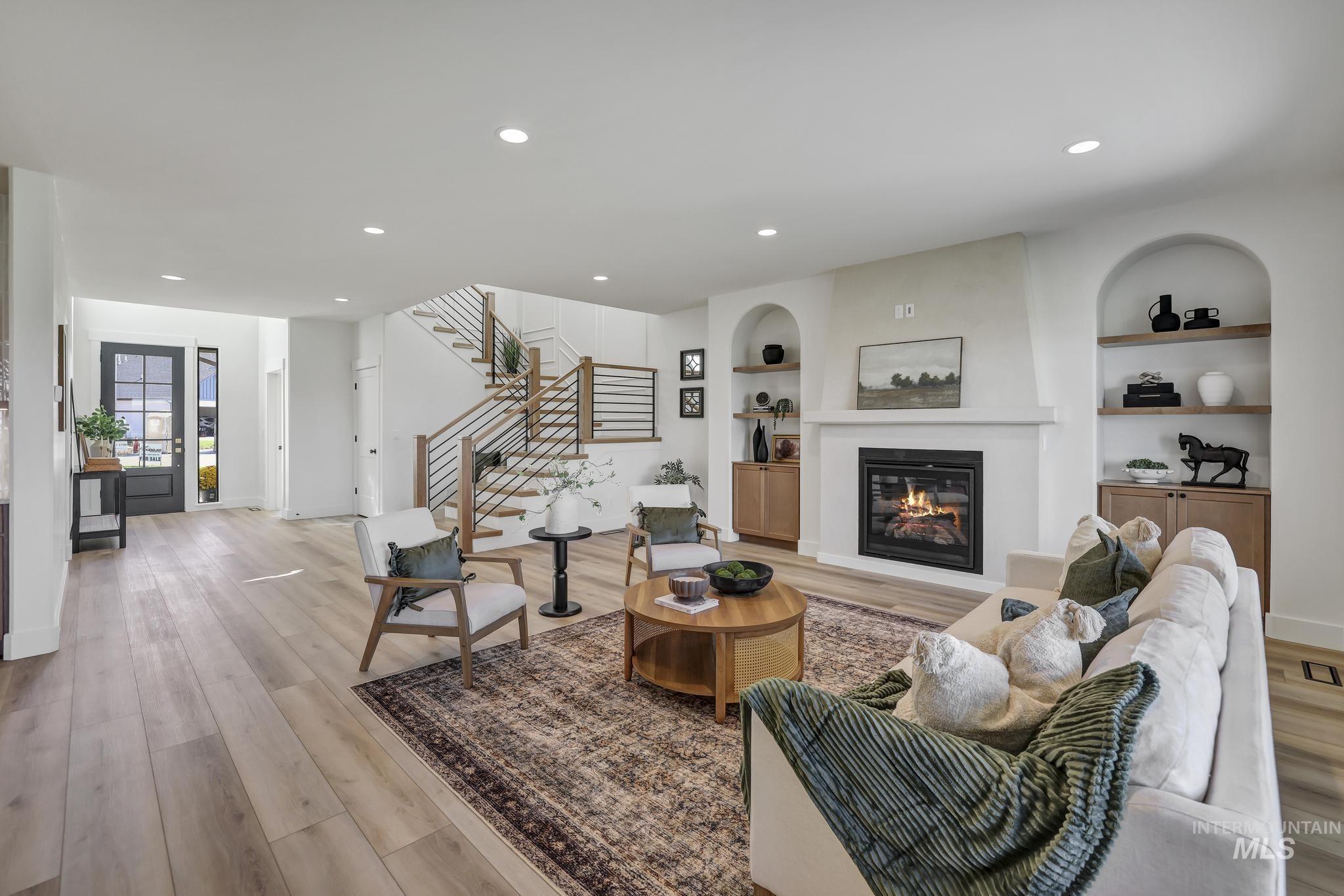 Living room with built in shelves, recessed lighting, a glass covered fireplace, light wood finished floors, and stairs