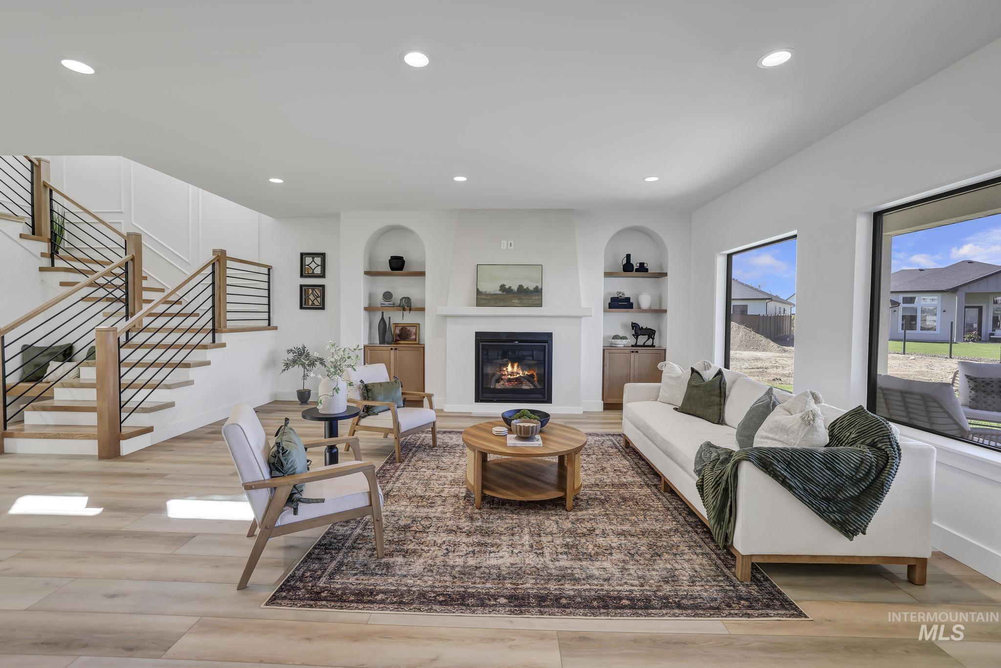 Living area featuring built in features, recessed lighting, a glass covered fireplace, stairs, and light wood-style flooring