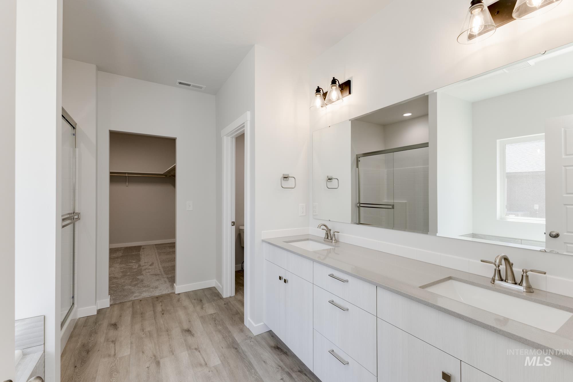 Bathroom with a shower stall, double vanity, a spacious closet, and wood finished floors
