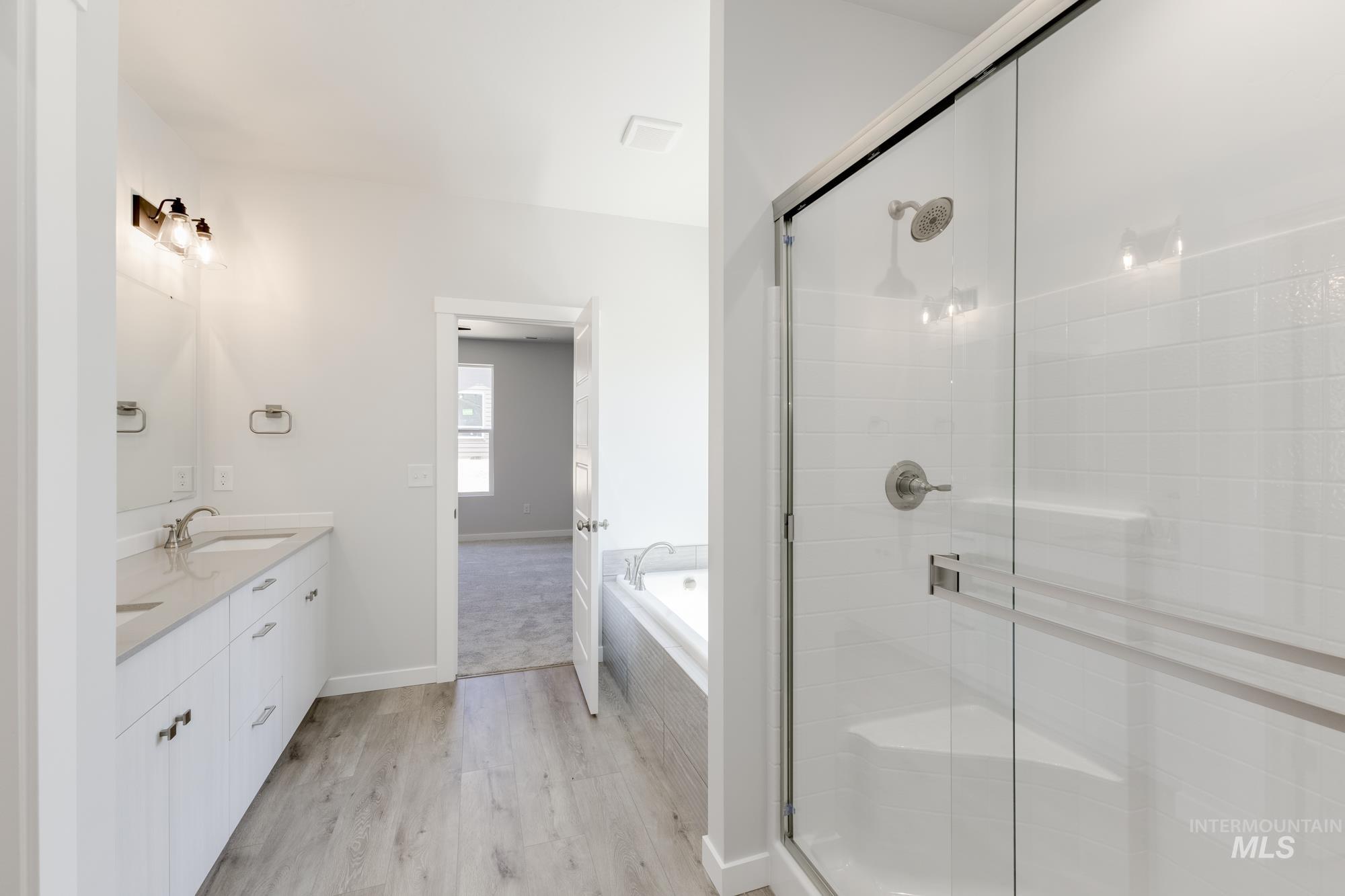 Bathroom with double vanity, wood finished floors, a stall shower, and a bath