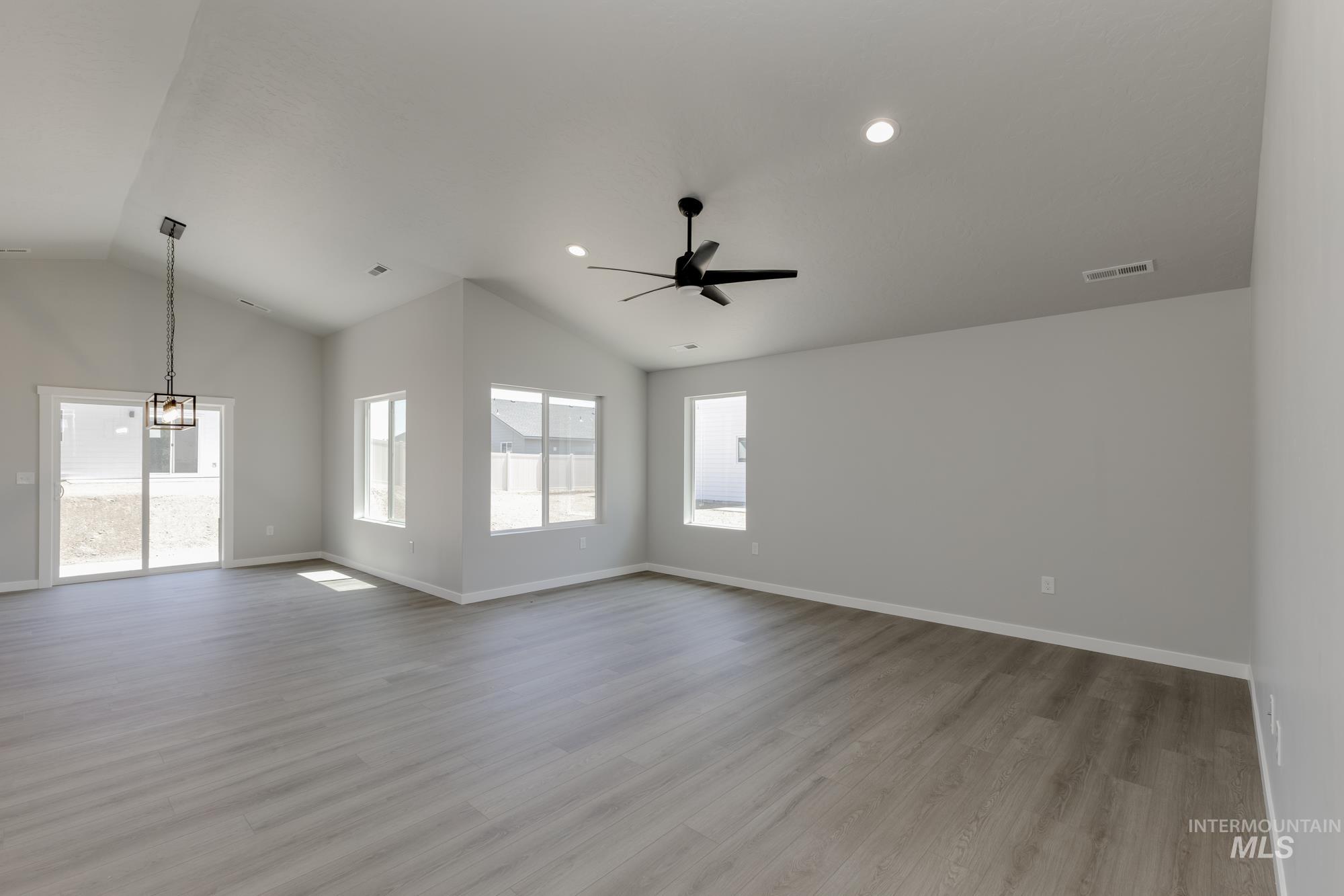 Unfurnished living room with lofted ceiling, healthy amount of natural light, a ceiling fan, wood finished floors, and a chandelier