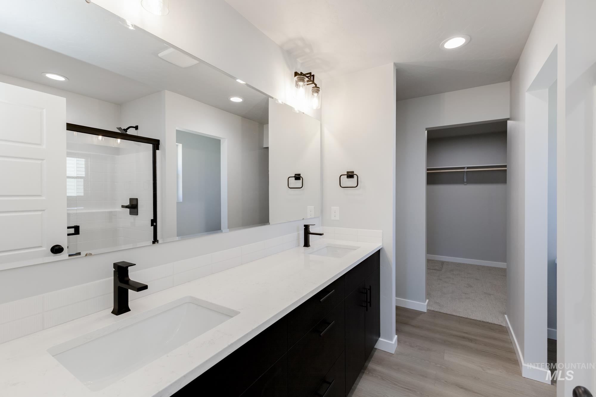 Bathroom with double vanity, a shower, wood finished floors, a spacious closet, and recessed lighting