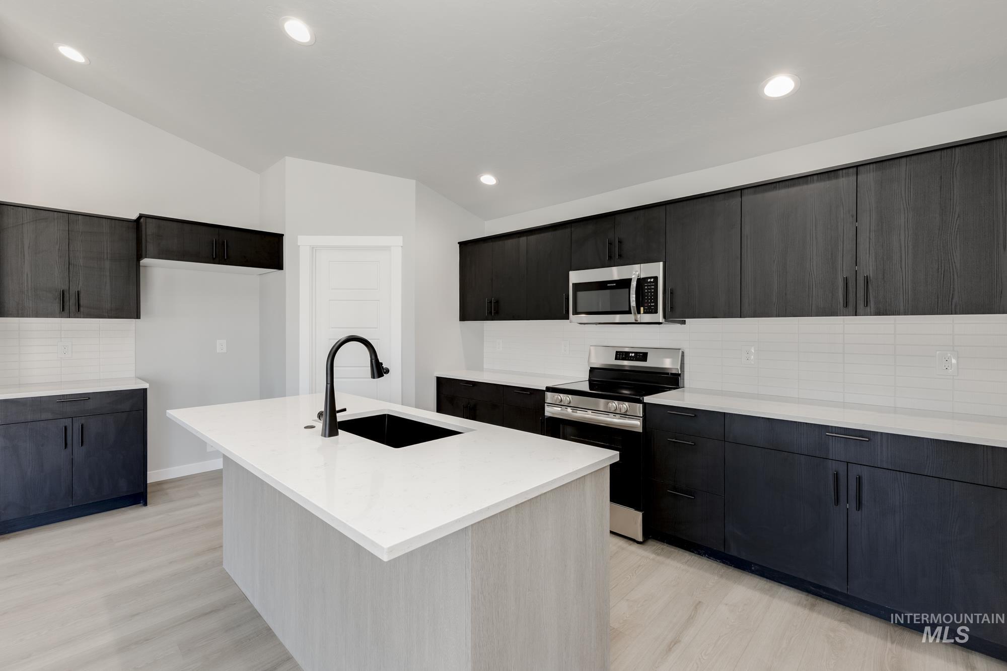 Kitchen featuring stainless steel appliances, vaulted ceiling, tasteful backsplash, light wood finished floors, and light countertops