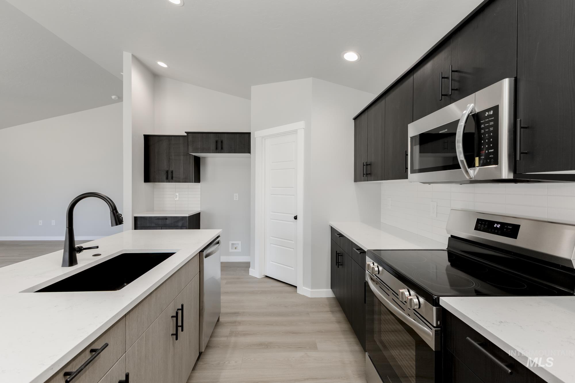 Kitchen featuring stainless steel appliances, tasteful backsplash, light wood-style flooring, recessed lighting, and dark cabinetry