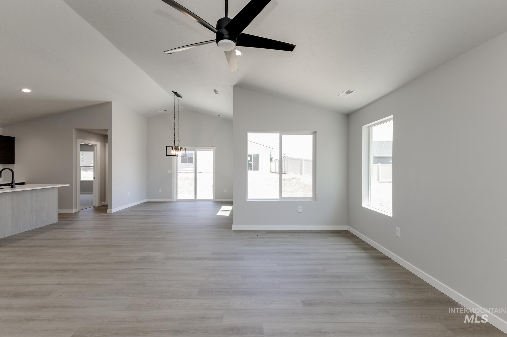 Unfurnished living room featuring lofted ceiling, a ceiling fan, and light wood-style flooring