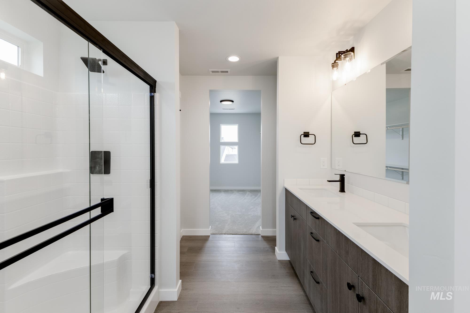 Bathroom featuring double vanity, a stall shower, and wood finished floors