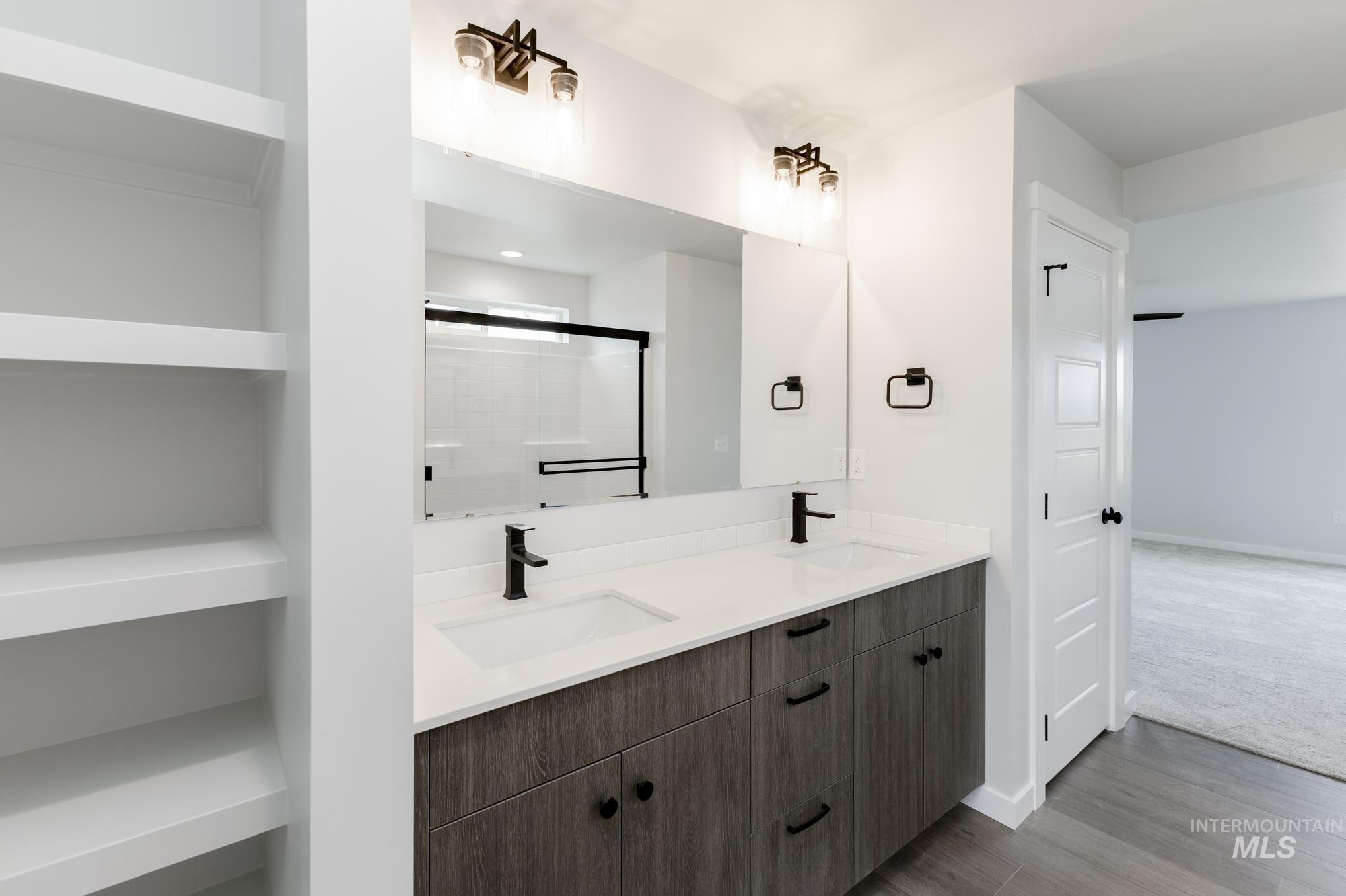Full bath featuring double vanity, wood finished floors, and an enclosed shower