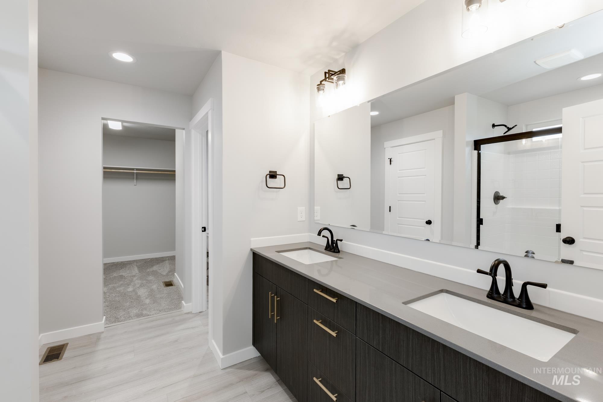 Bathroom with double vanity, a walk in closet, a tile shower, wood finished floors, and recessed lighting