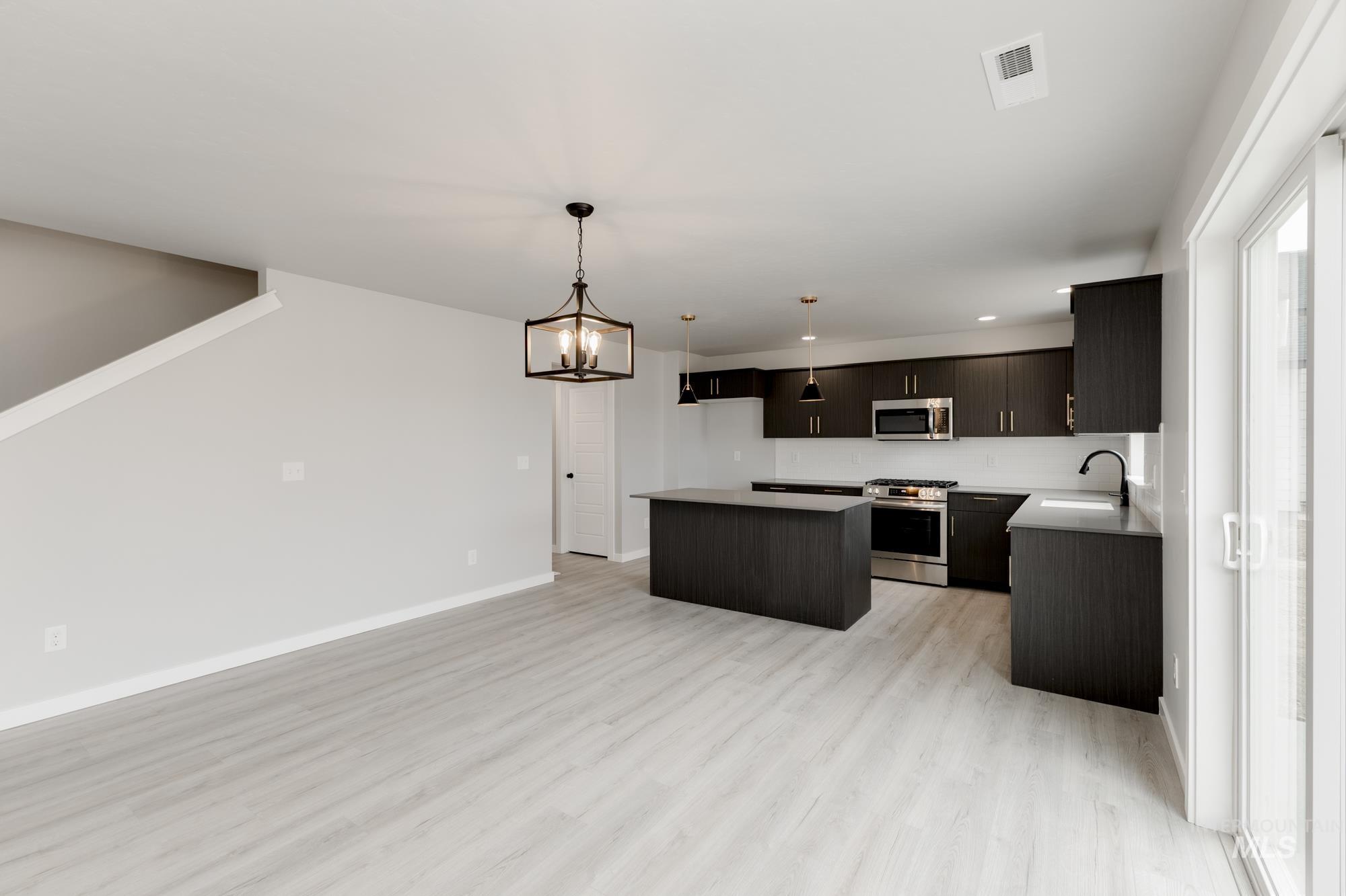 Kitchen with stainless steel appliances, a kitchen island, light wood-style flooring, a chandelier, and open floor plan
