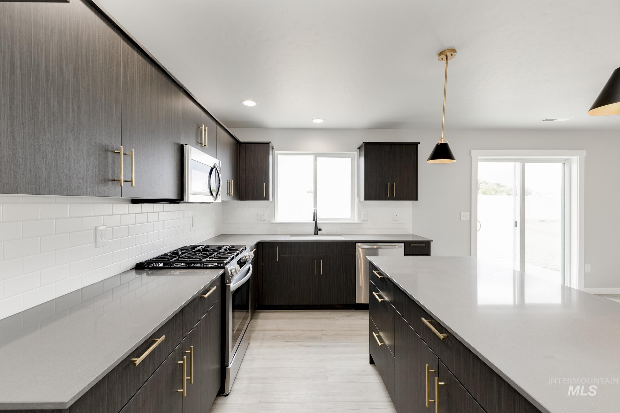 Kitchen featuring appliances with stainless steel finishes, backsplash, decorative light fixtures, light countertops, and light wood-type flooring