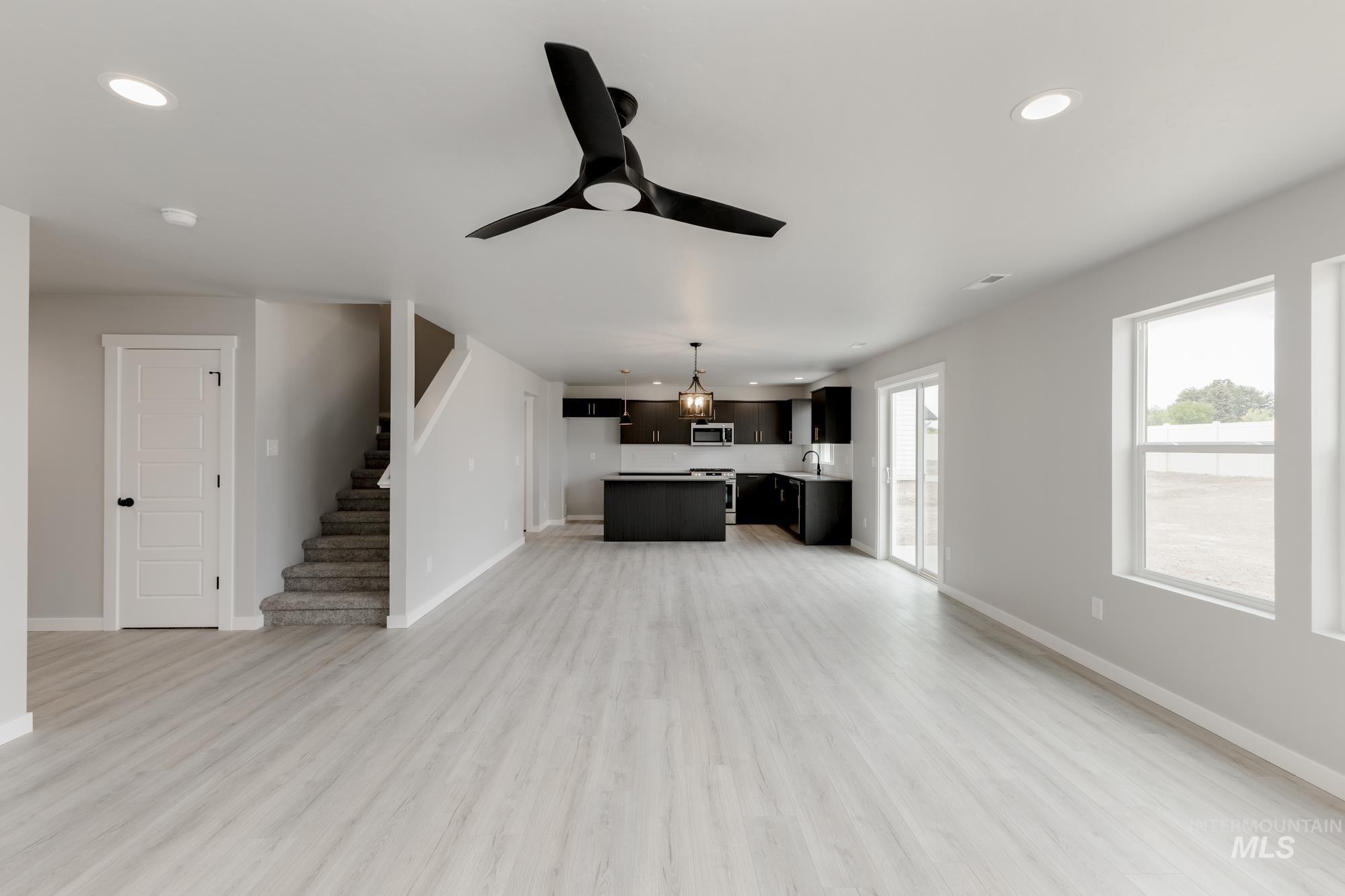 Unfurnished living room featuring ceiling fan, light wood-style flooring, recessed lighting, and stairs