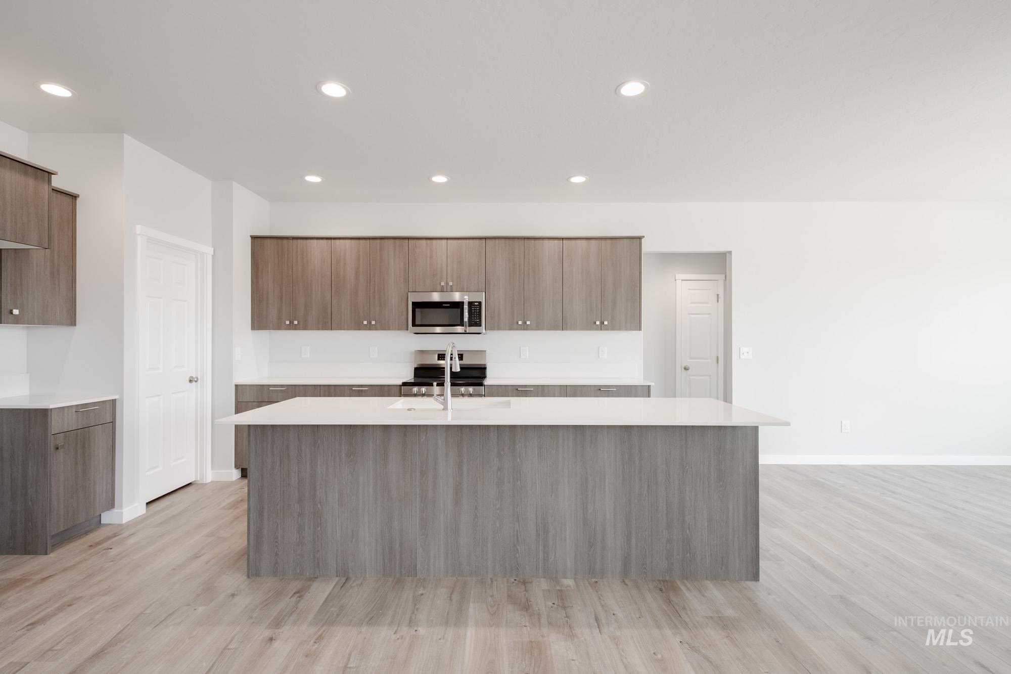 Kitchen with stainless steel microwave, modern cabinets, light countertops, a kitchen island with sink, and light wood-style floors
