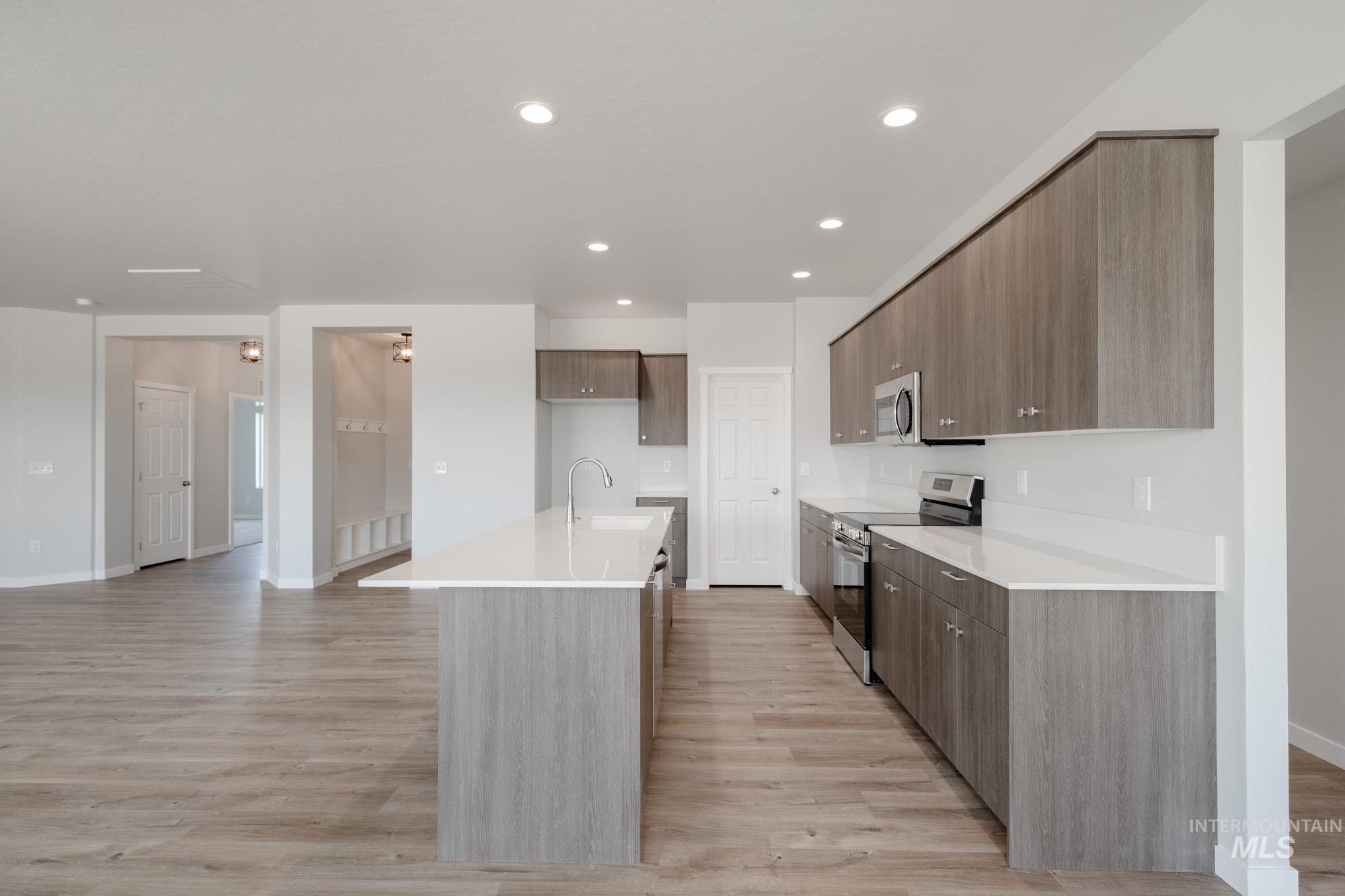 Kitchen with appliances with stainless steel finishes, light wood finished floors, light countertops, recessed lighting, and an island with sink
