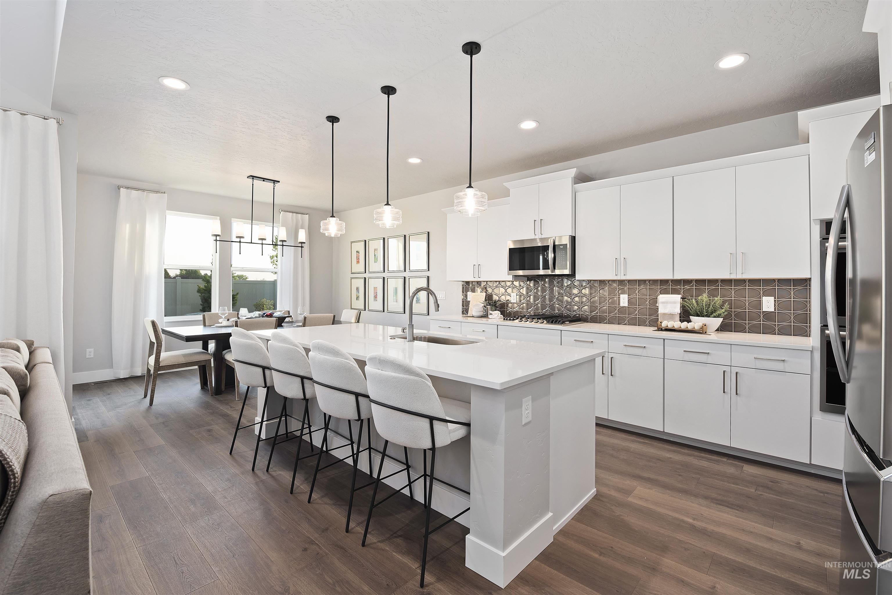 Kitchen featuring decorative backsplash, a breakfast bar area, an island with sink, white cabinetry, and hanging light fixtures