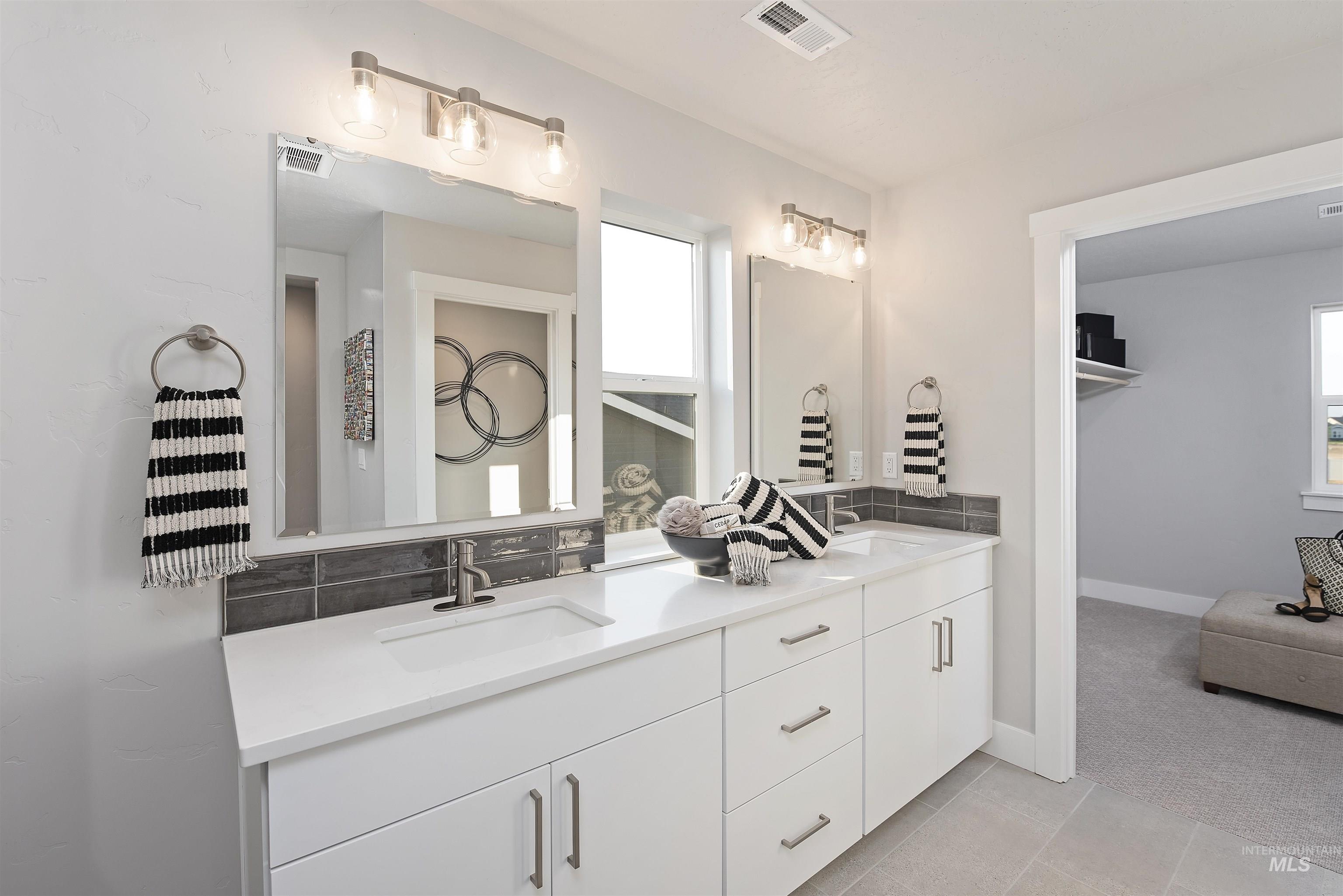 Bathroom with double vanity, light tile patterned floors, and decorative backsplash