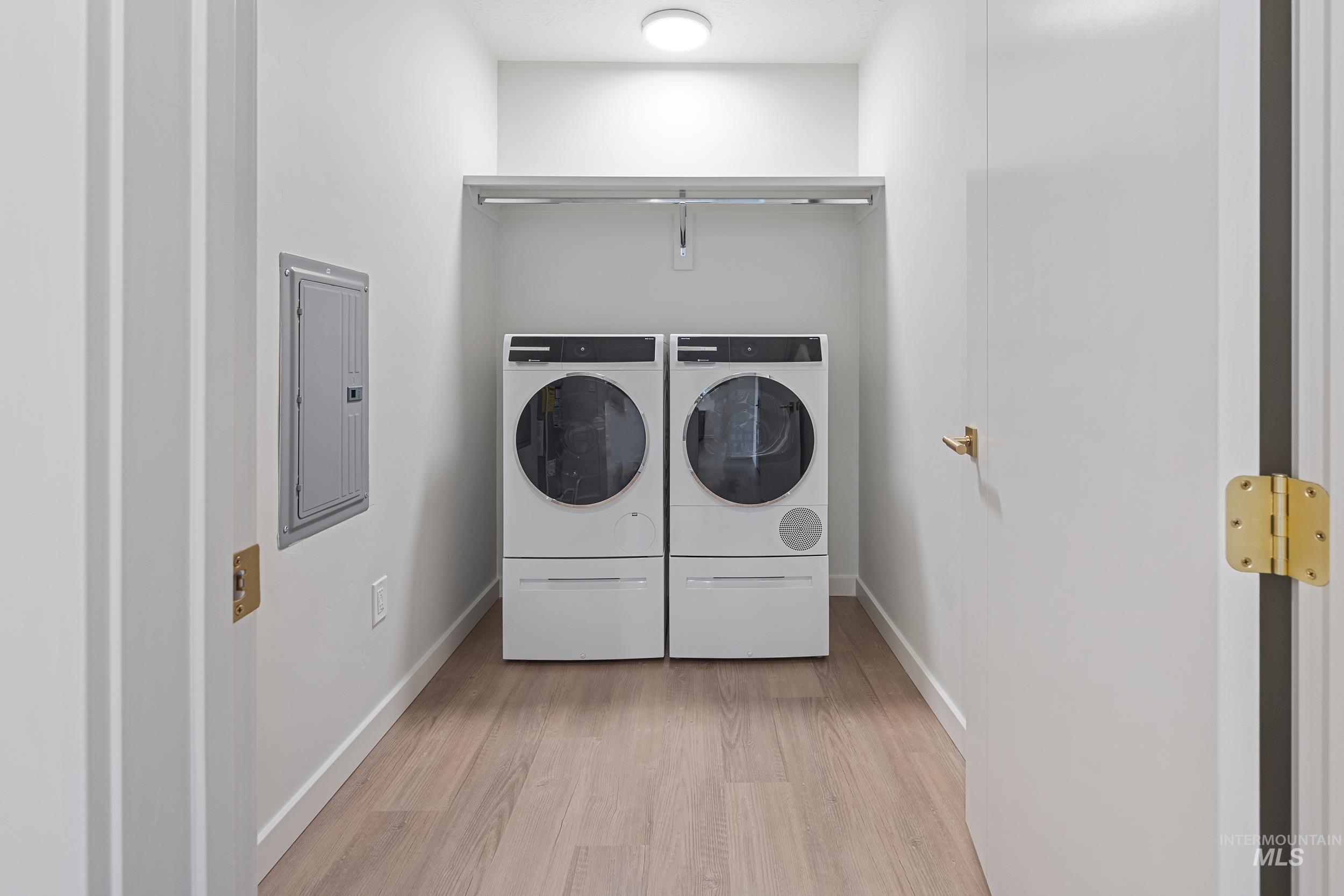 Laundry area with light wood finished floors, electric panel, and washer and dryer
