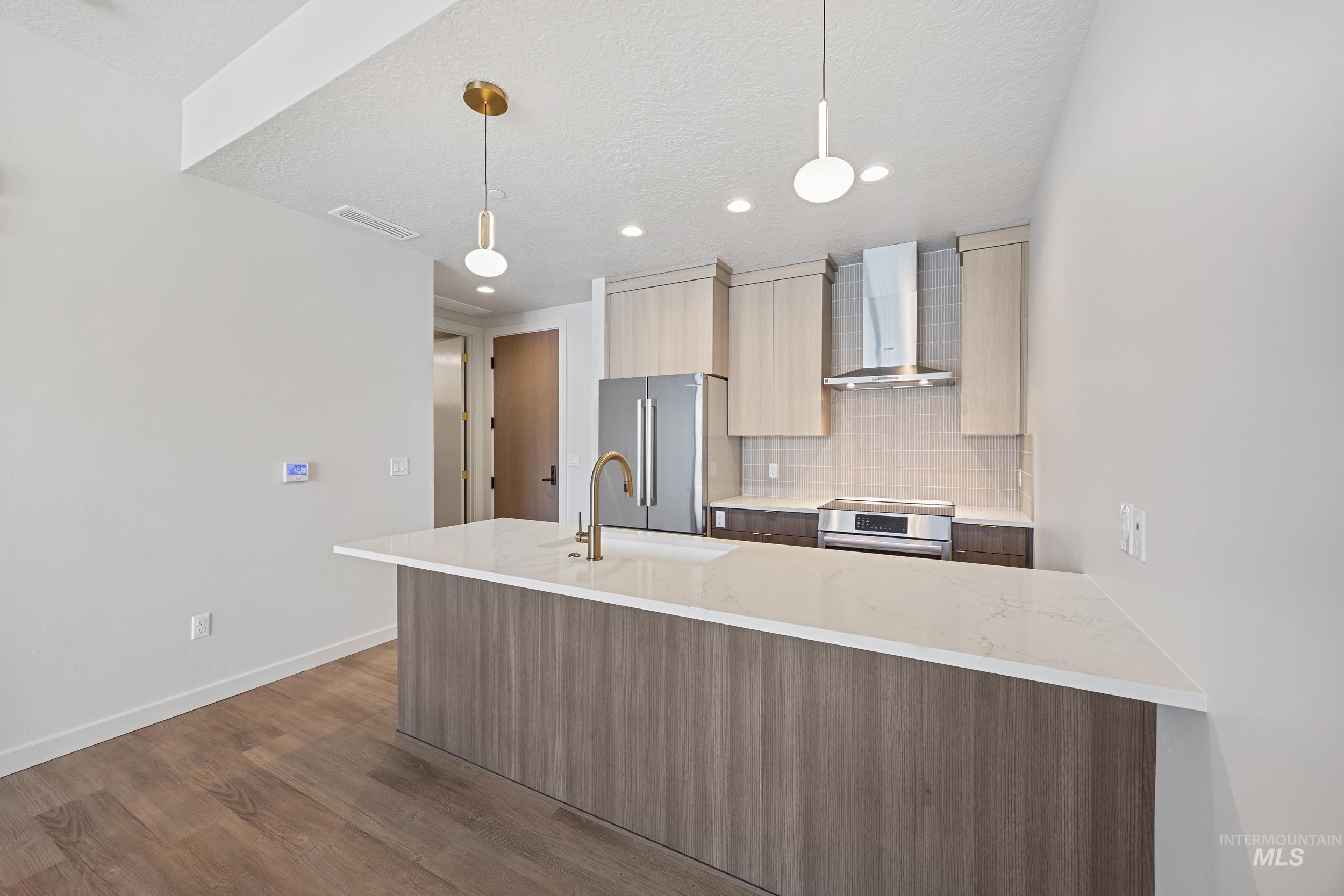 Kitchen with modern cabinets, tasteful backsplash, light stone counters, wall chimney exhaust hood, and dark wood-style floors