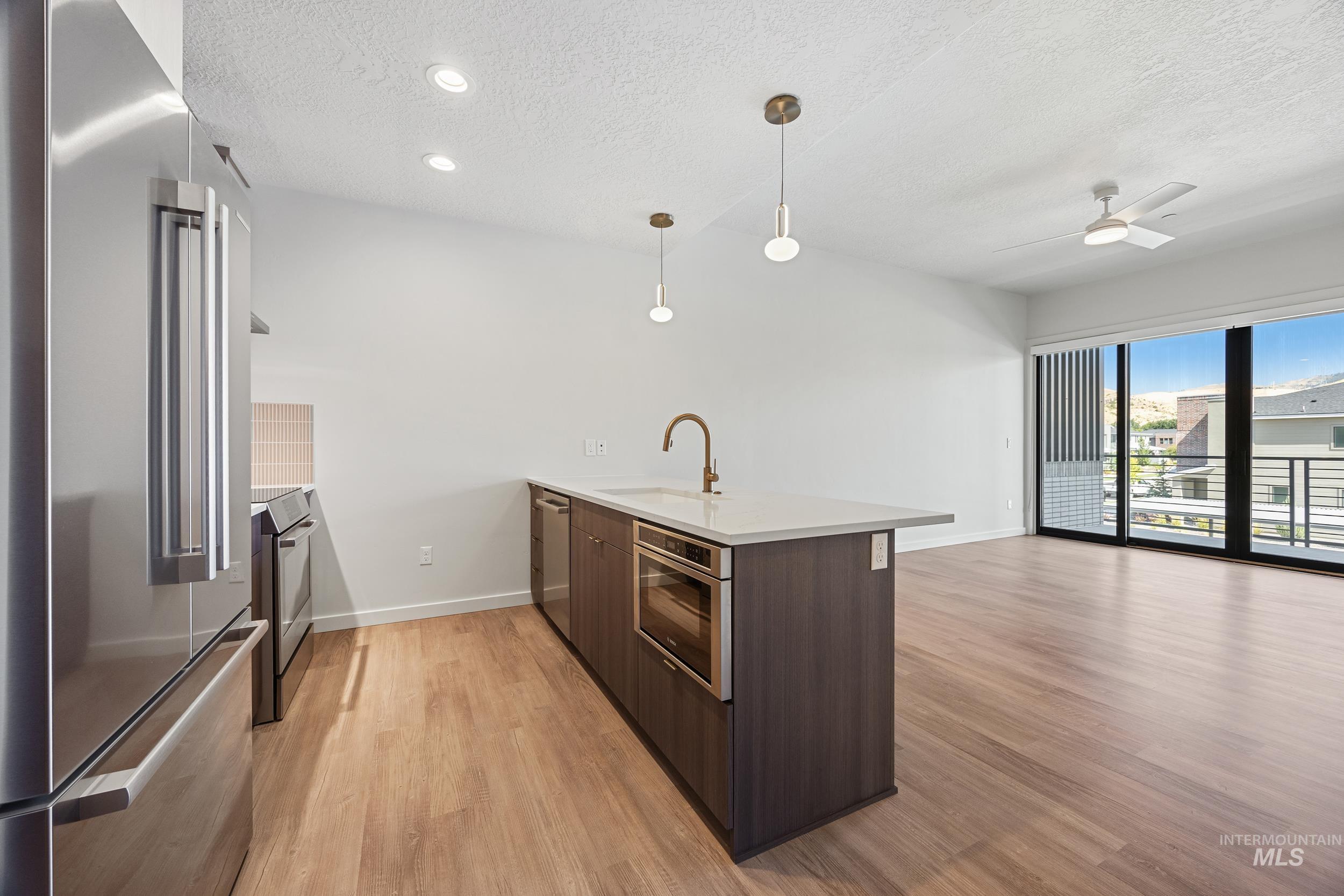Kitchen with a peninsula, stainless steel appliances, dark brown cabinetry, modern cabinets, and light wood-style floors