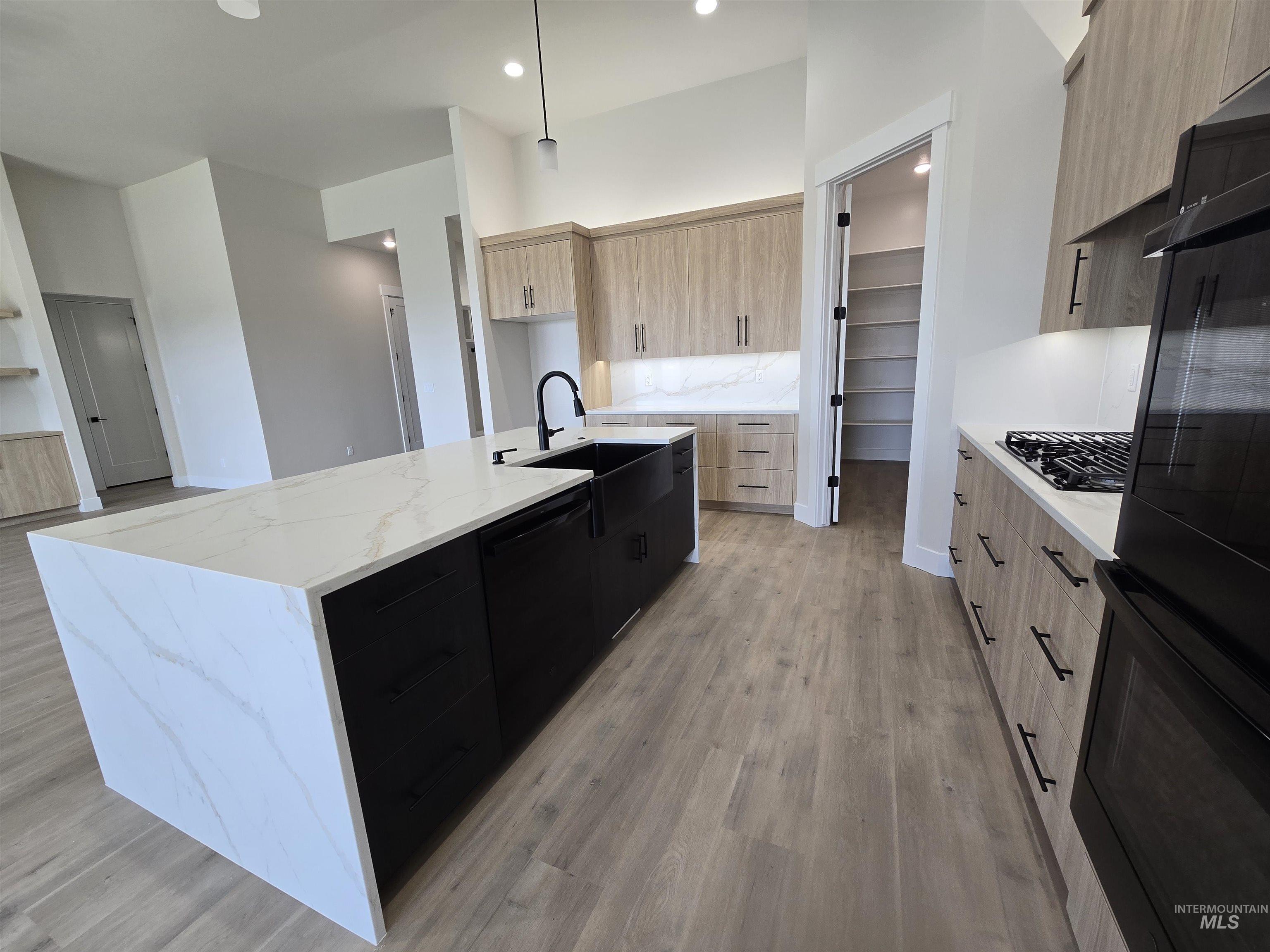 Kitchen featuring modern cabinets, light brown cabinets, a large island with sink, black appliances, and recessed lighting