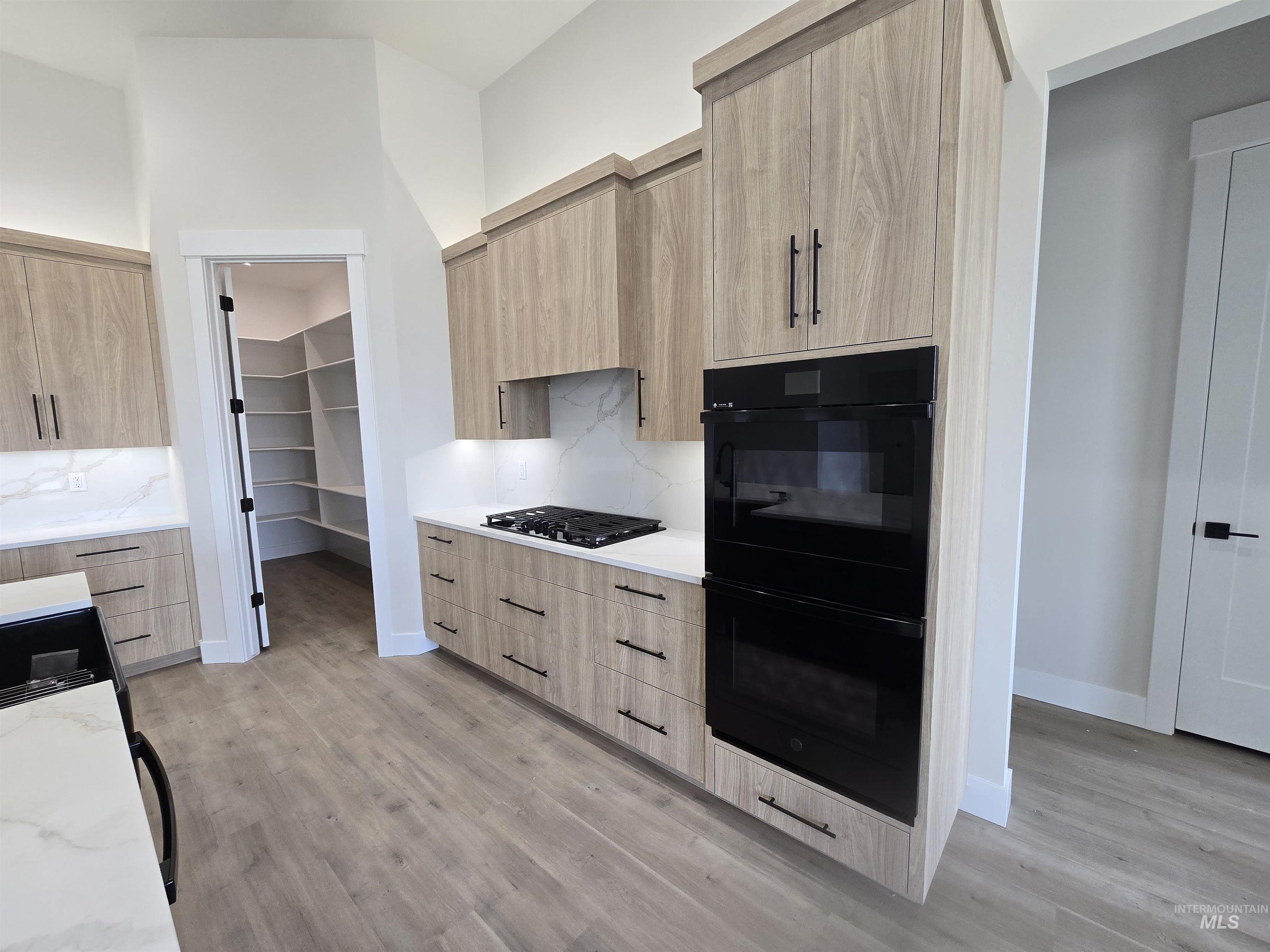 Kitchen featuring light brown cabinetry, modern cabinets, black appliances, light stone countertops, and light wood-type flooring