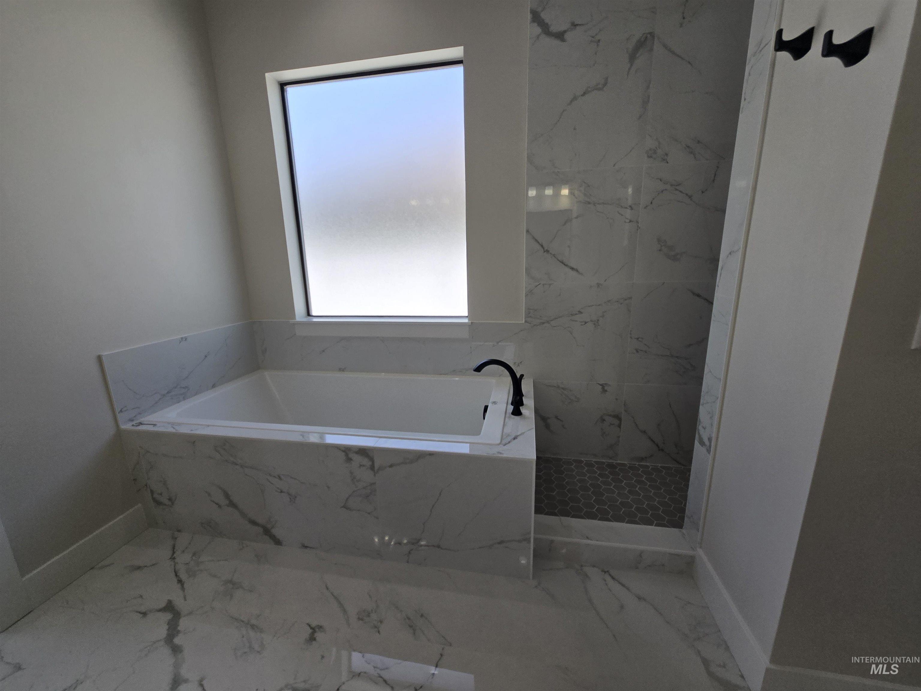 Bathroom with marble look tiles, a garden tub, and a marble finish shower