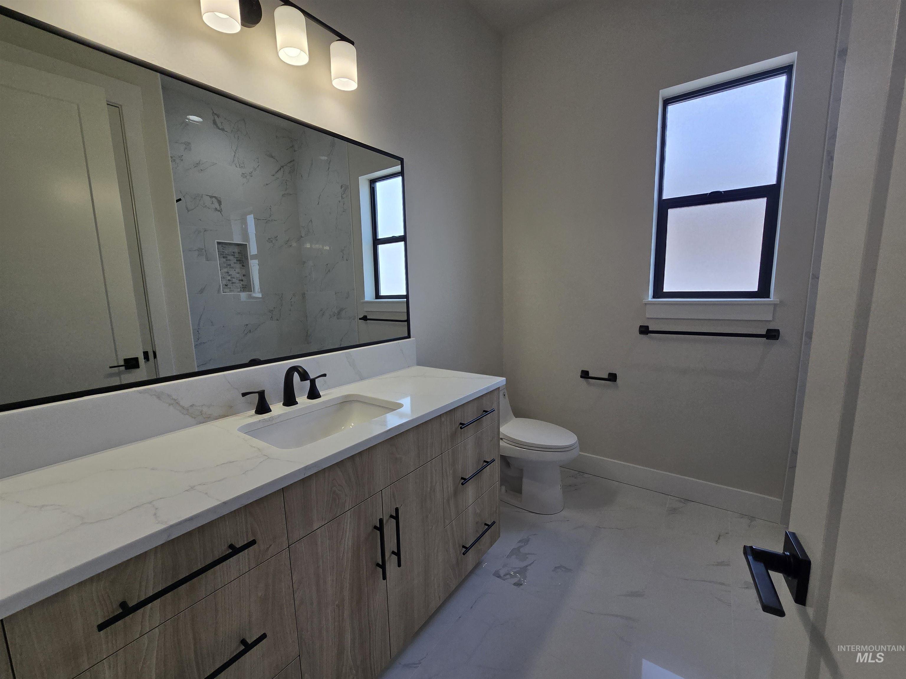 Full bath featuring marble look tiles, vanity, and plenty of natural light