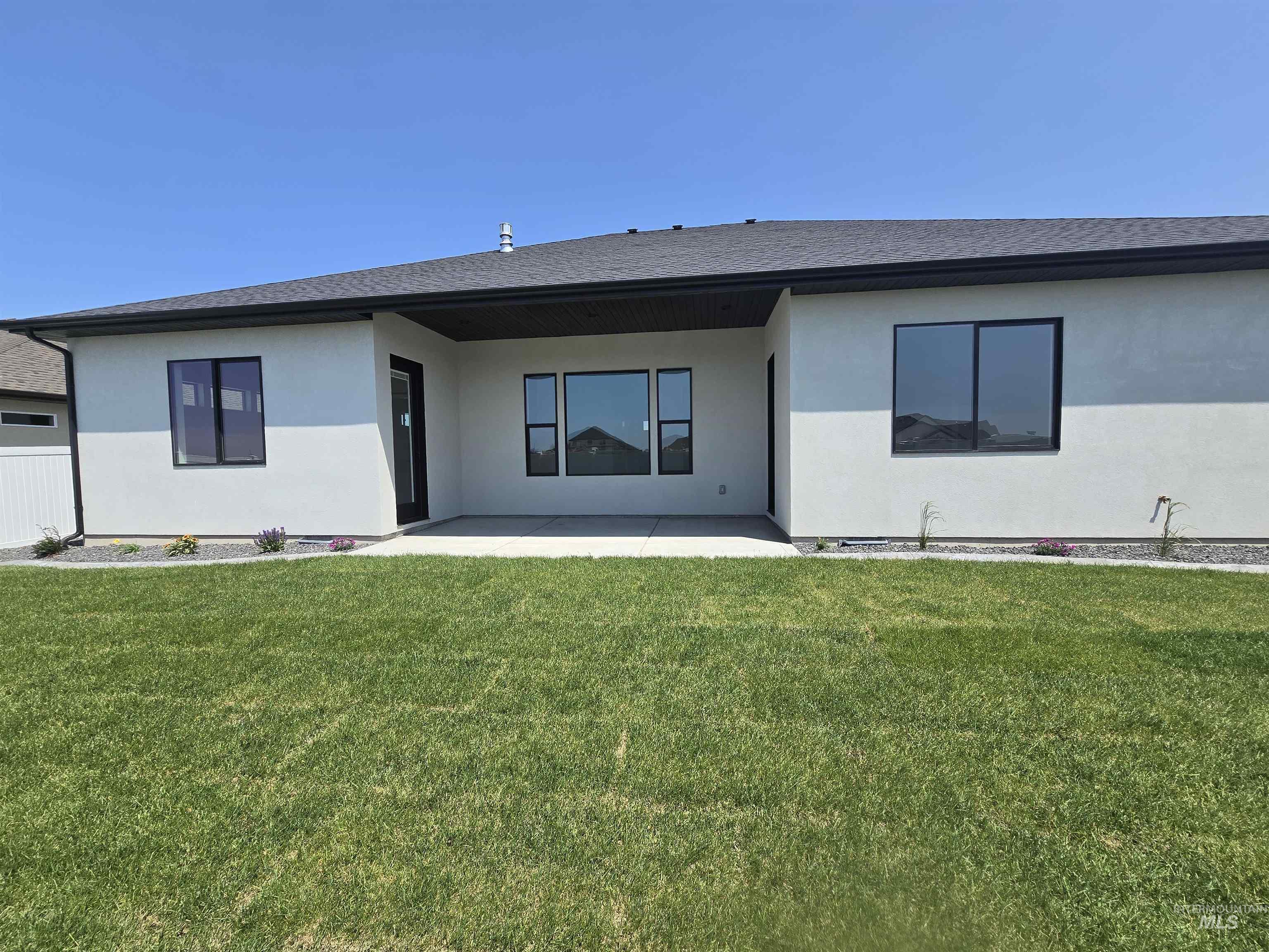 Back of property with a patio, a lawn, stucco siding, and roof with shingles