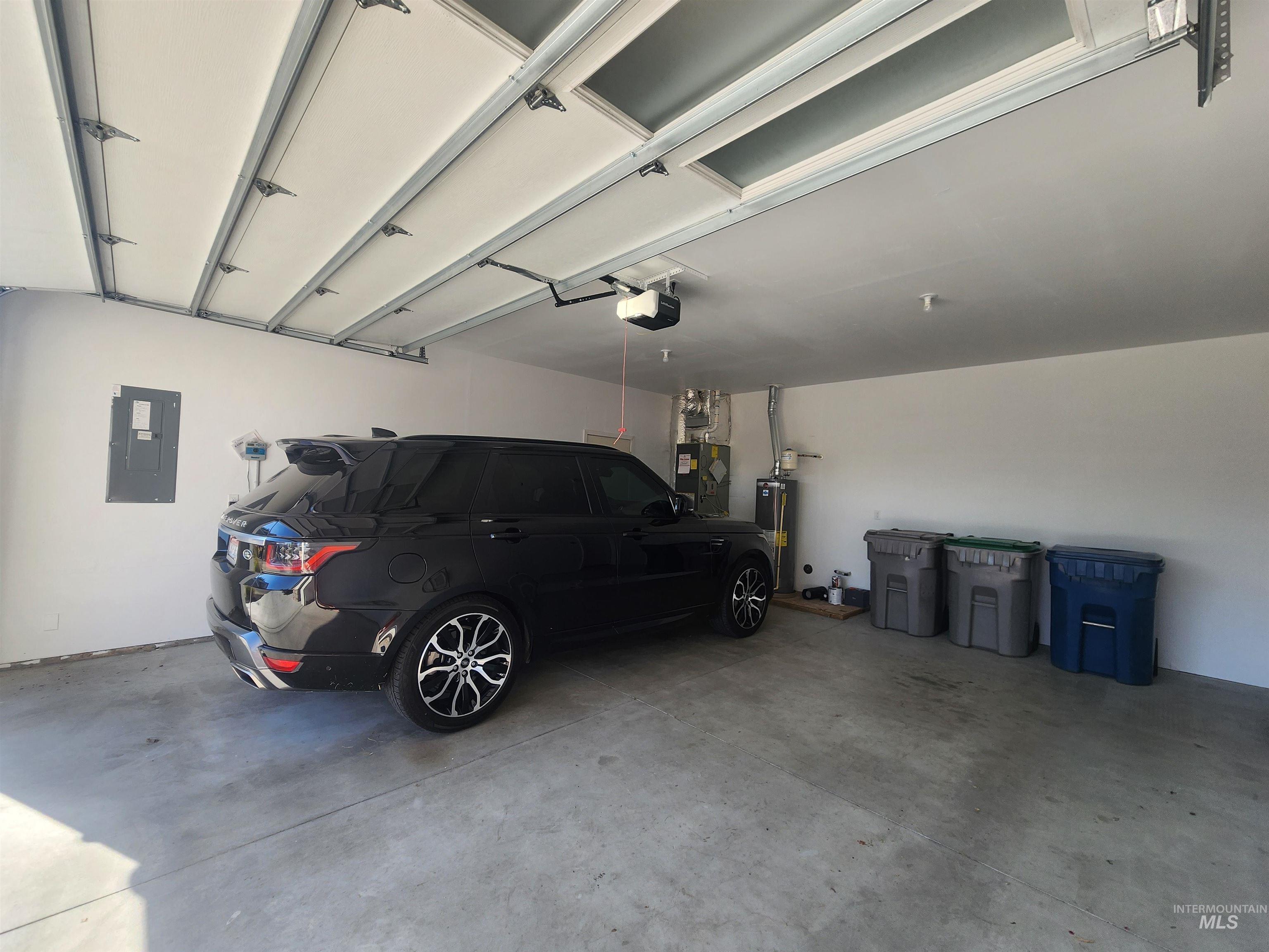 Garage featuring electric panel, gas water heater, heating unit, and a garage door opener