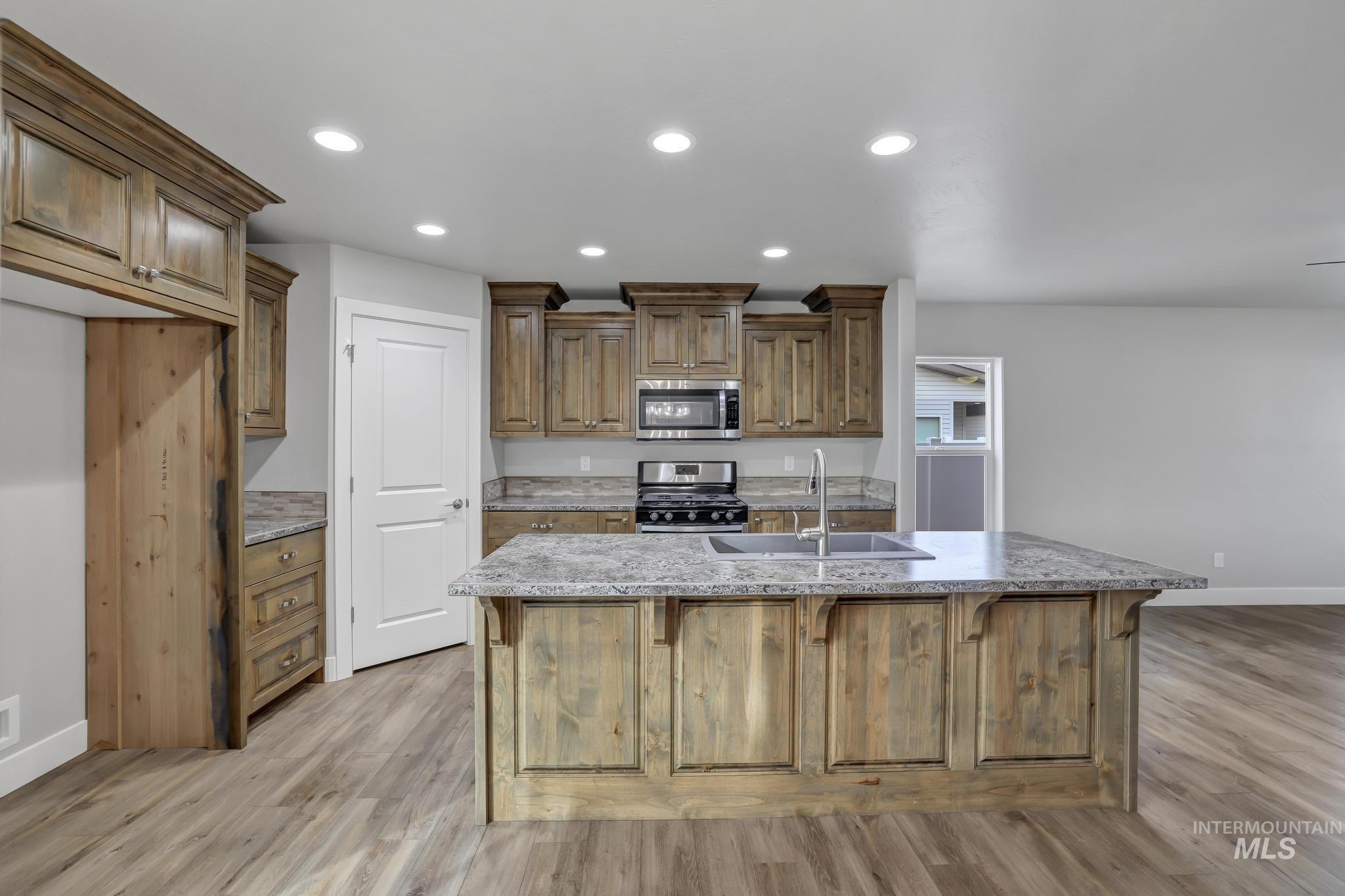 Kitchen featuring brown cabinets, light stone counters, appliances with stainless steel finishes, a breakfast bar, and a kitchen island with sink