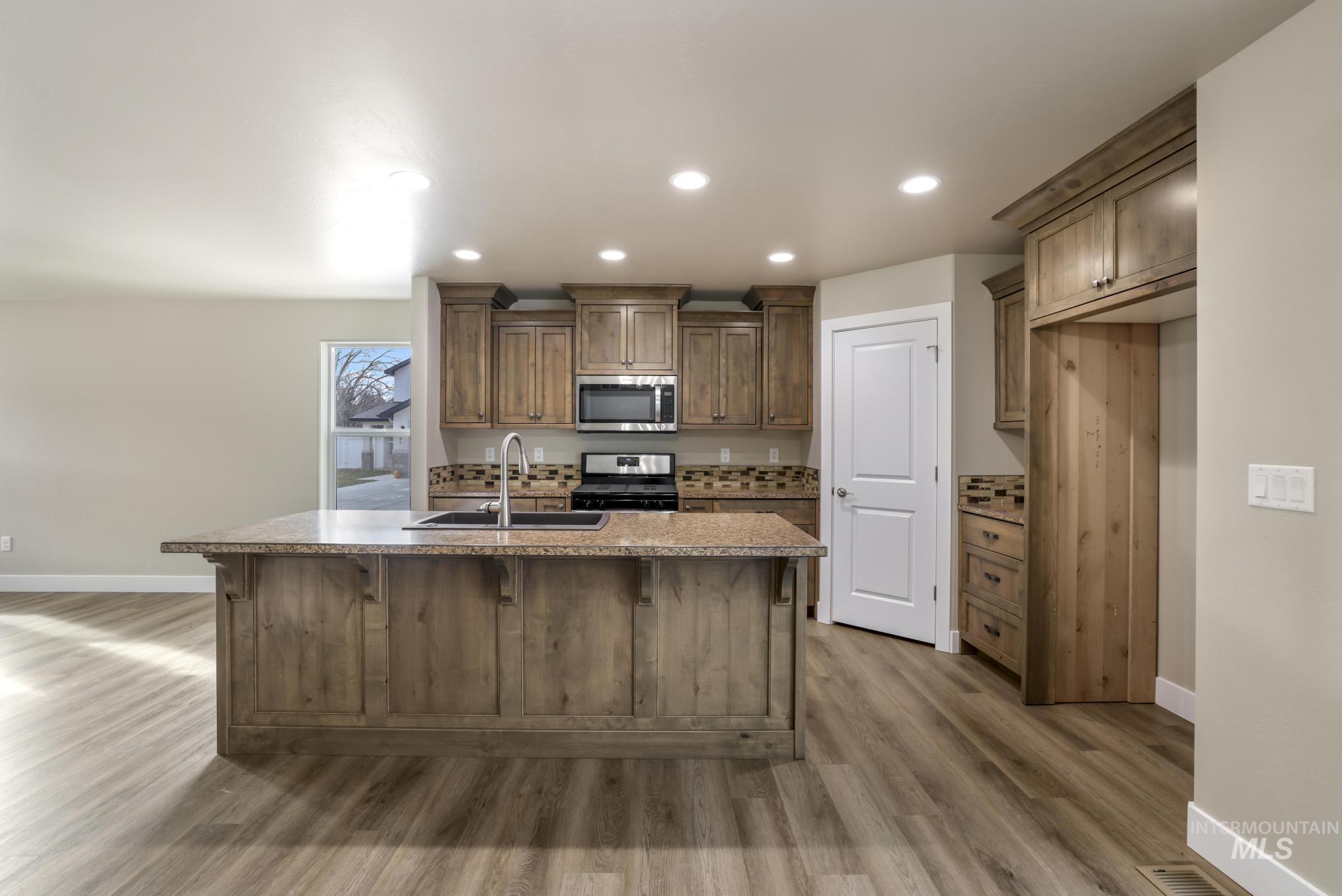 Kitchen with appliances with stainless steel finishes, an island with sink, recessed lighting, light wood finished floors, and a kitchen bar