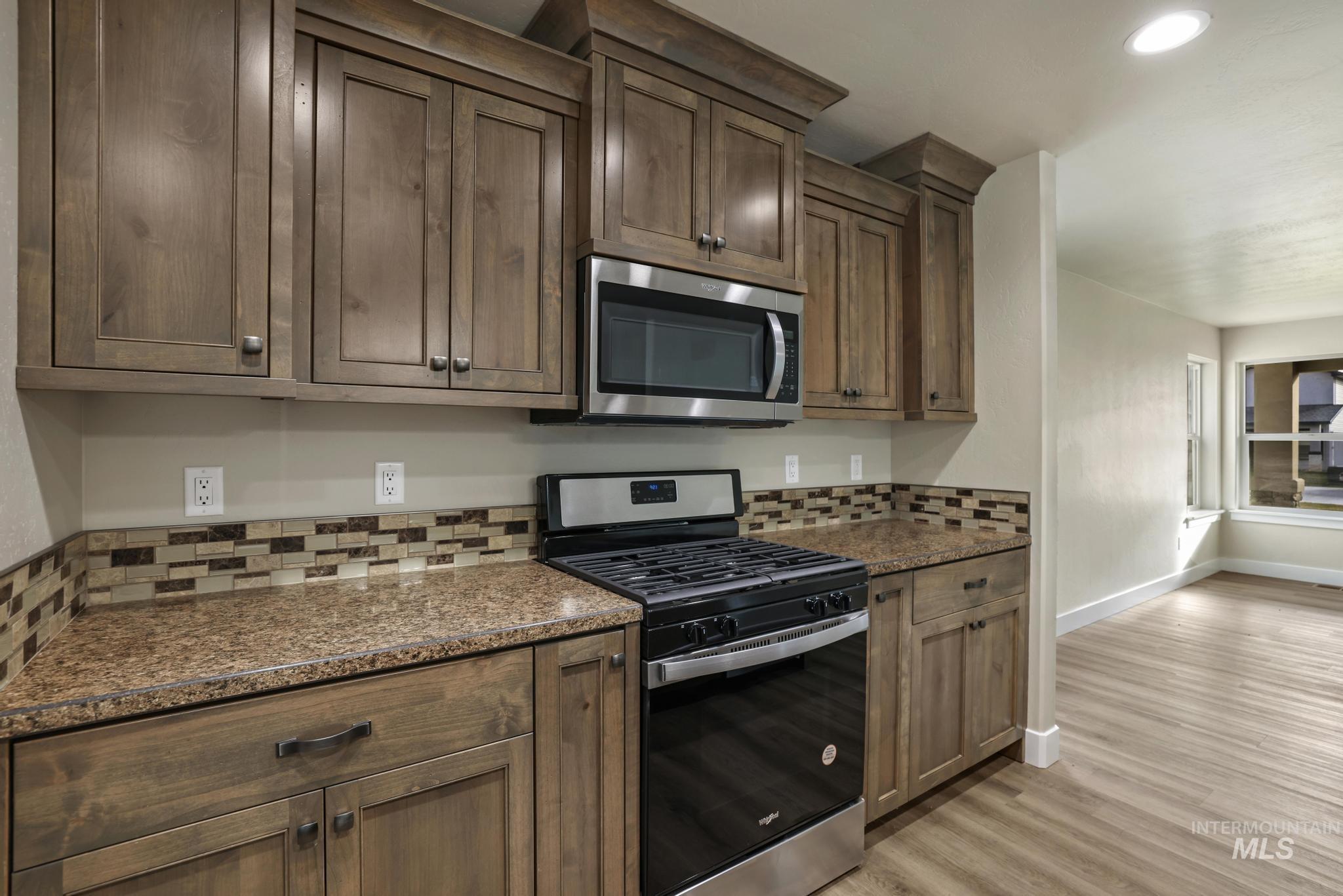 Kitchen with stainless steel appliances, dark stone countertops, light wood-style flooring, recessed lighting, and backsplash