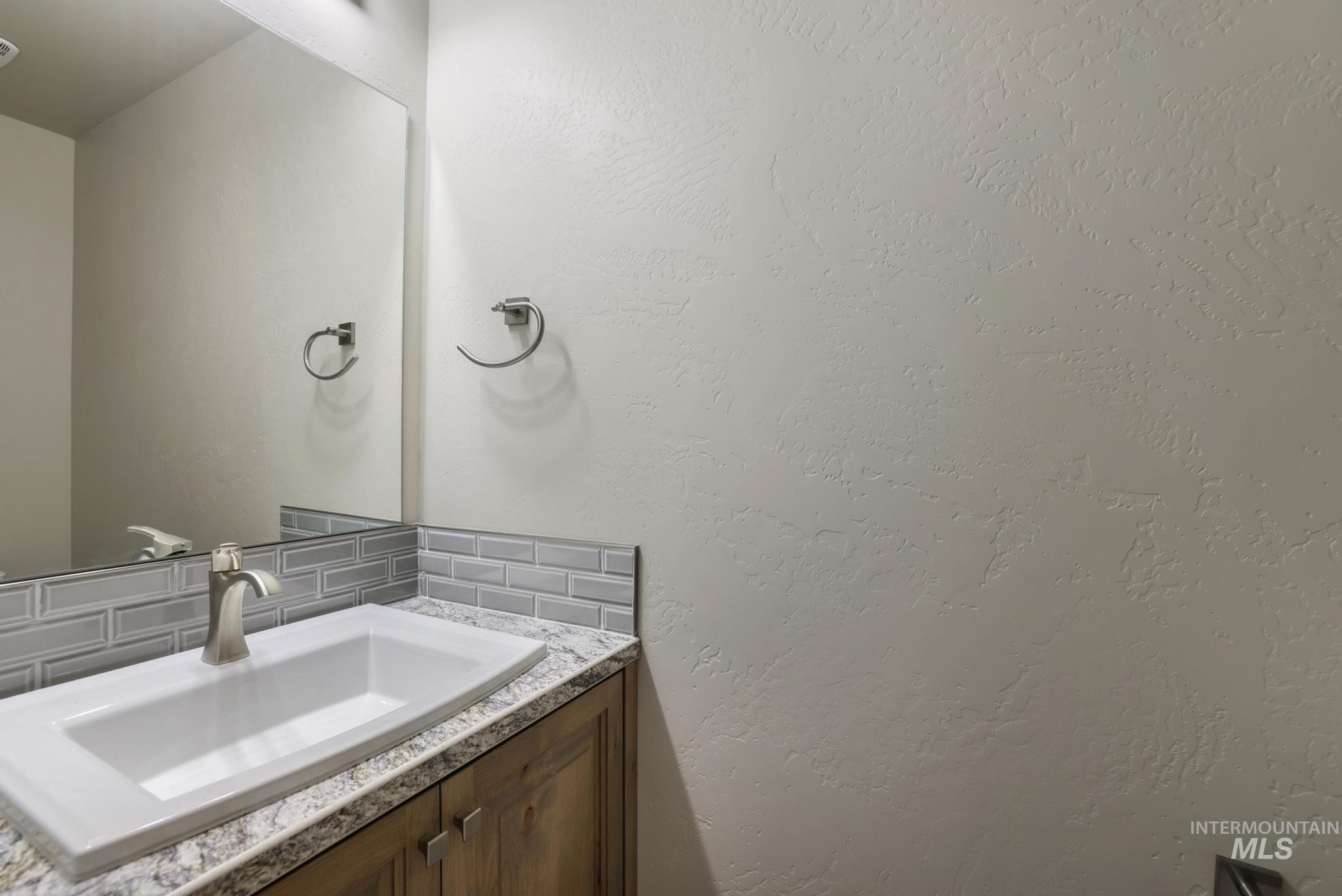Bathroom featuring decorative backsplash, a textured wall, and vanity