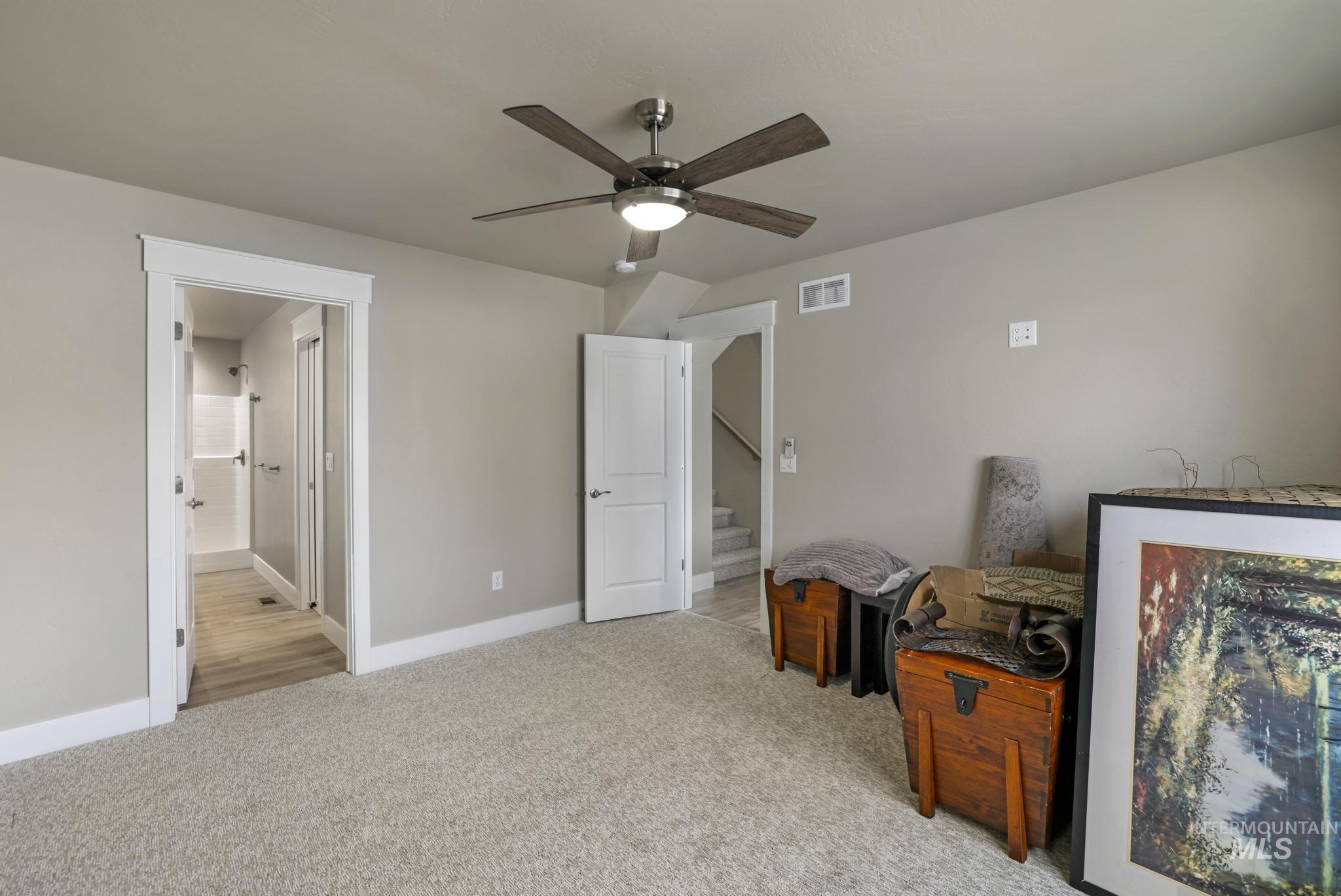 Unfurnished bedroom featuring light carpet, ceiling fan, and ensuite bath
