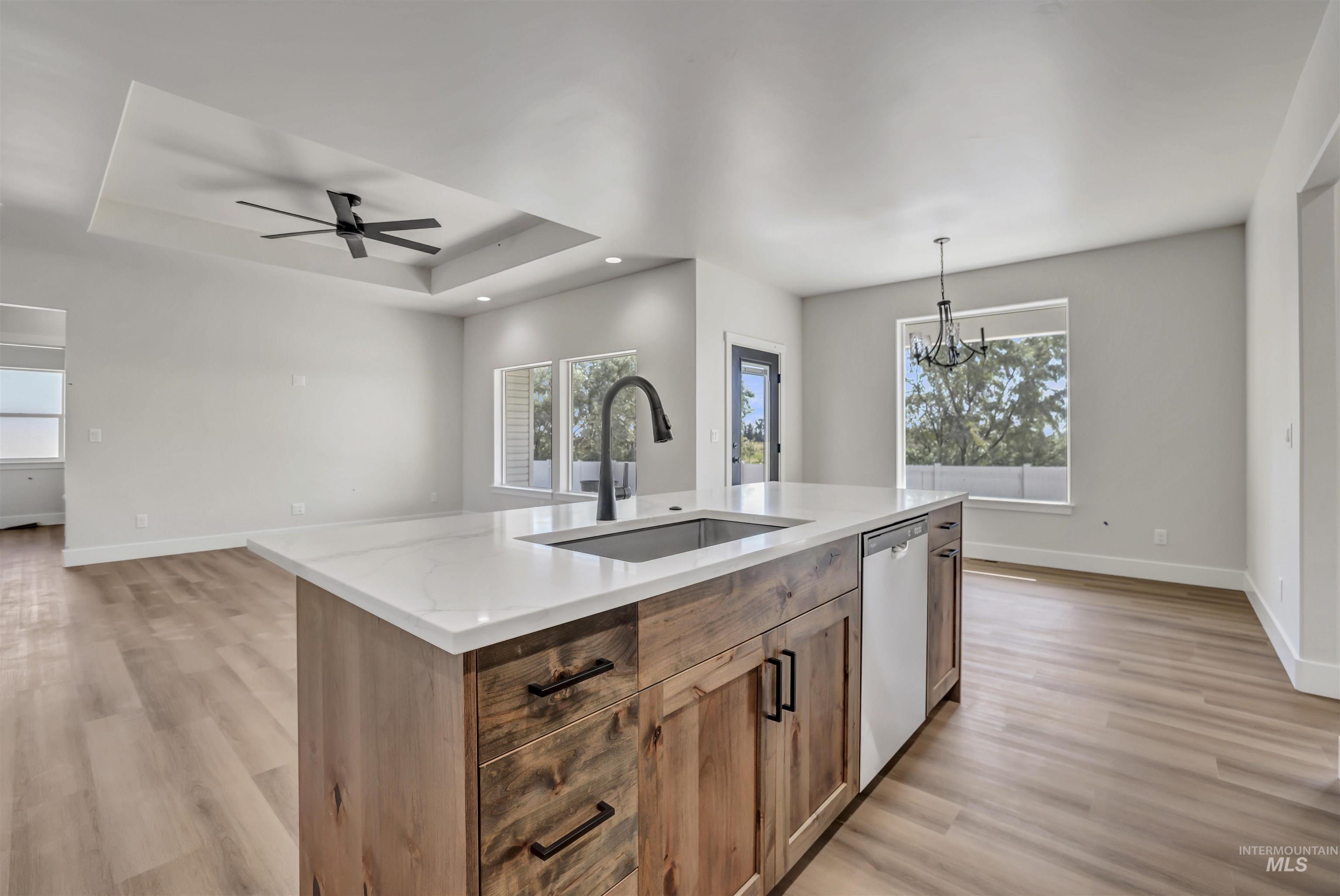 Kitchen featuring a chandelier, light wood-type flooring, dishwashing machine, a raised ceiling, and recessed lighting