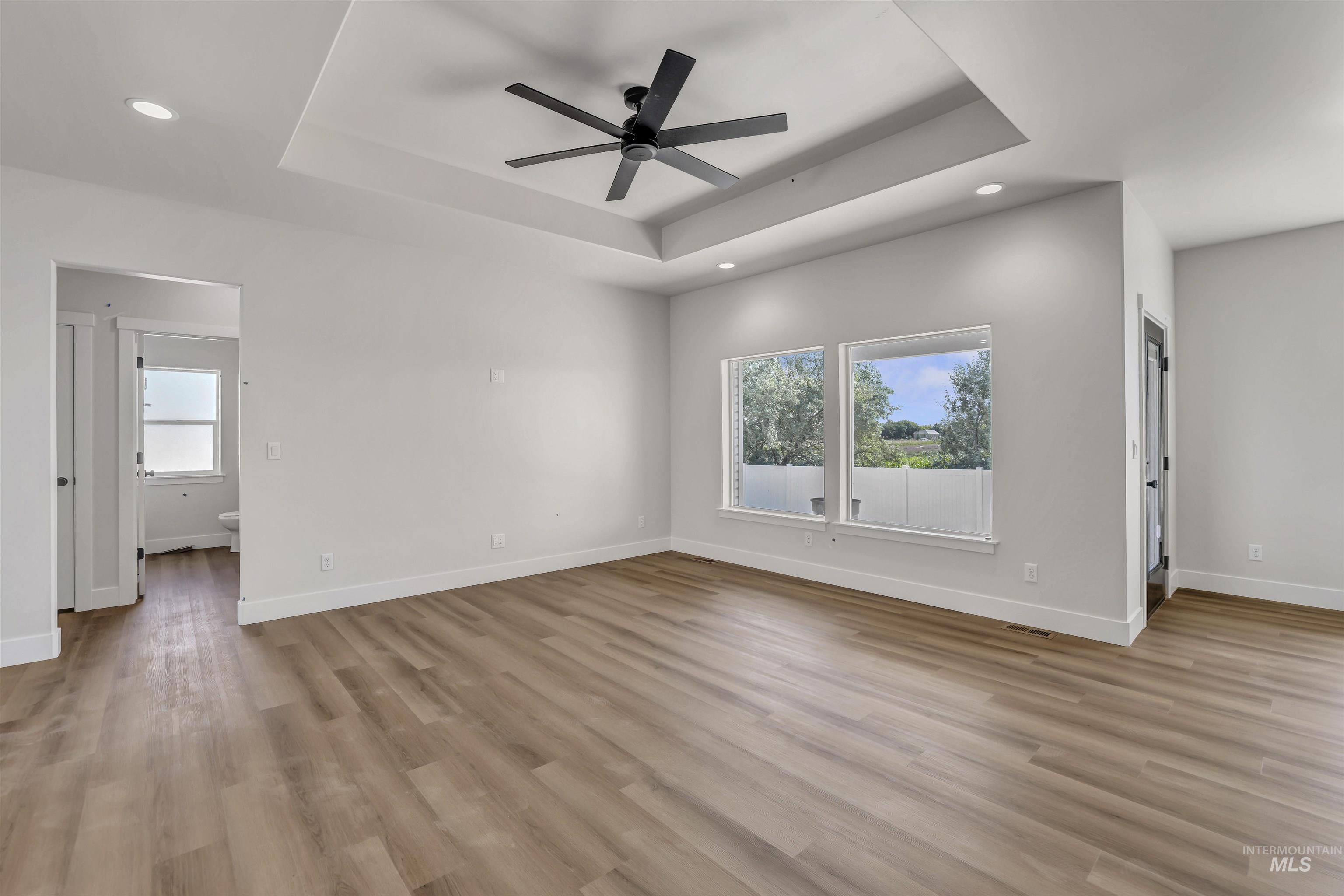 Unfurnished room featuring a raised ceiling, a ceiling fan, light wood-style flooring, and recessed lighting