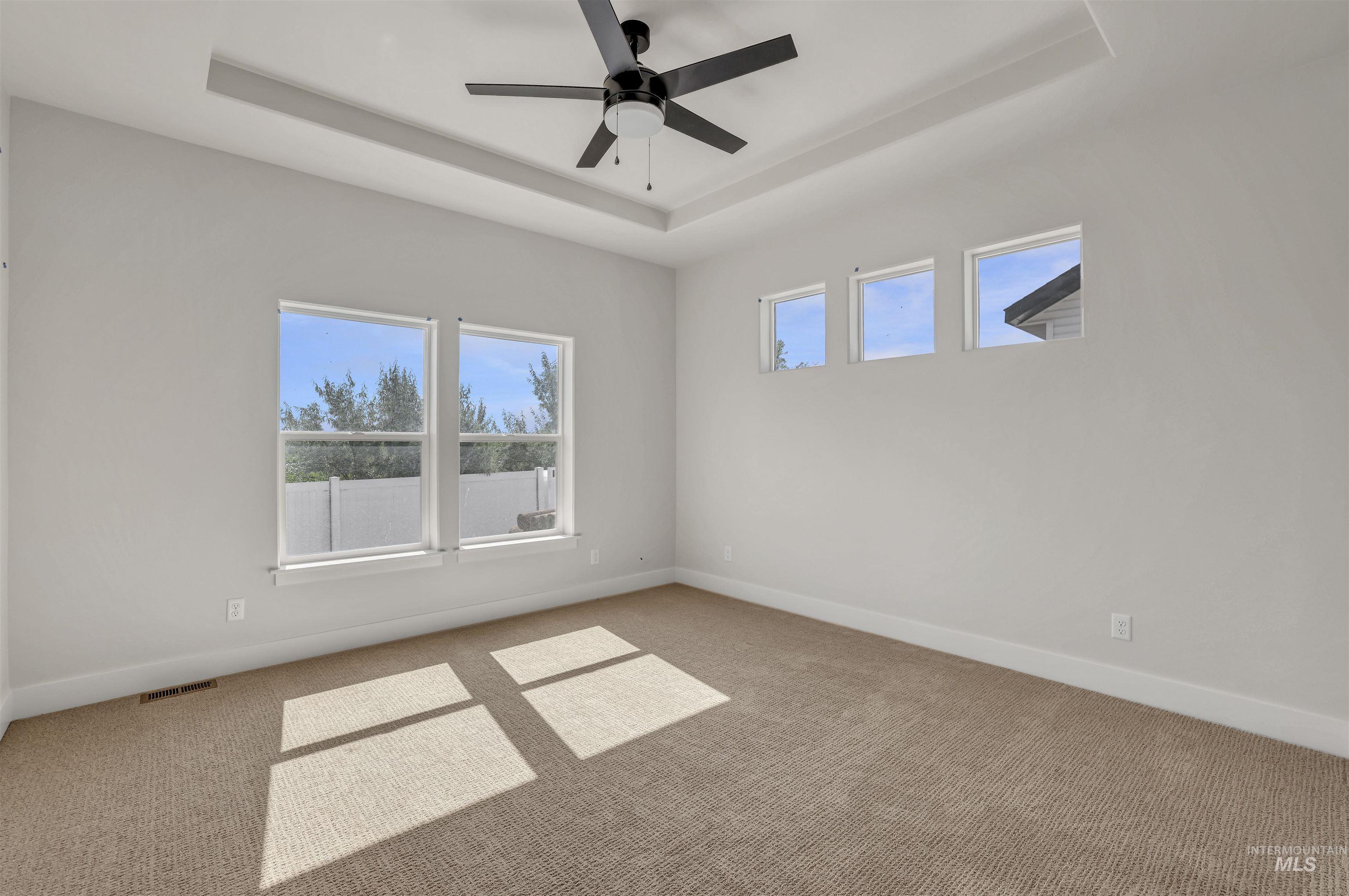 Empty room with a raised ceiling, carpet flooring, and a ceiling fan