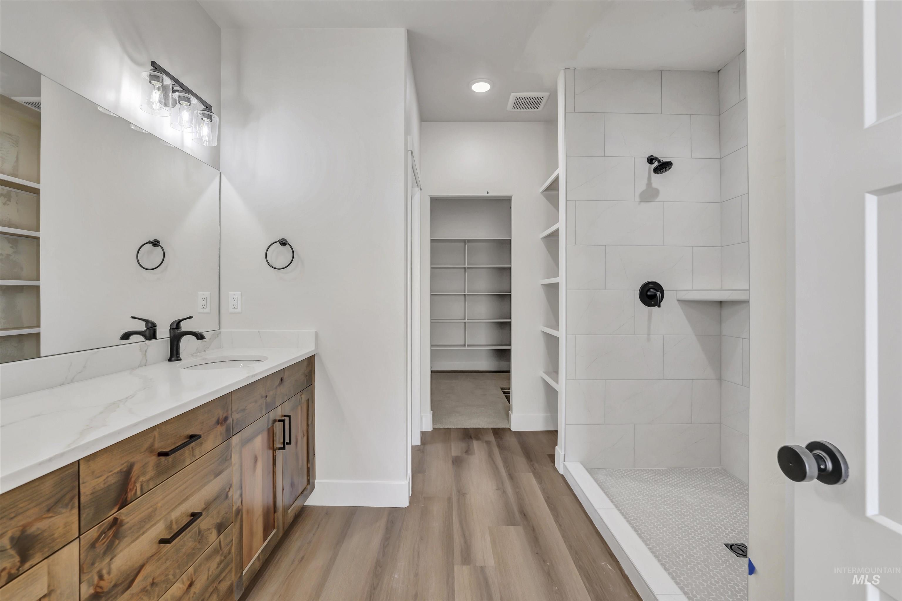 Bathroom featuring wood finished floors, vanity, a tile shower, a walk in closet, and recessed lighting
