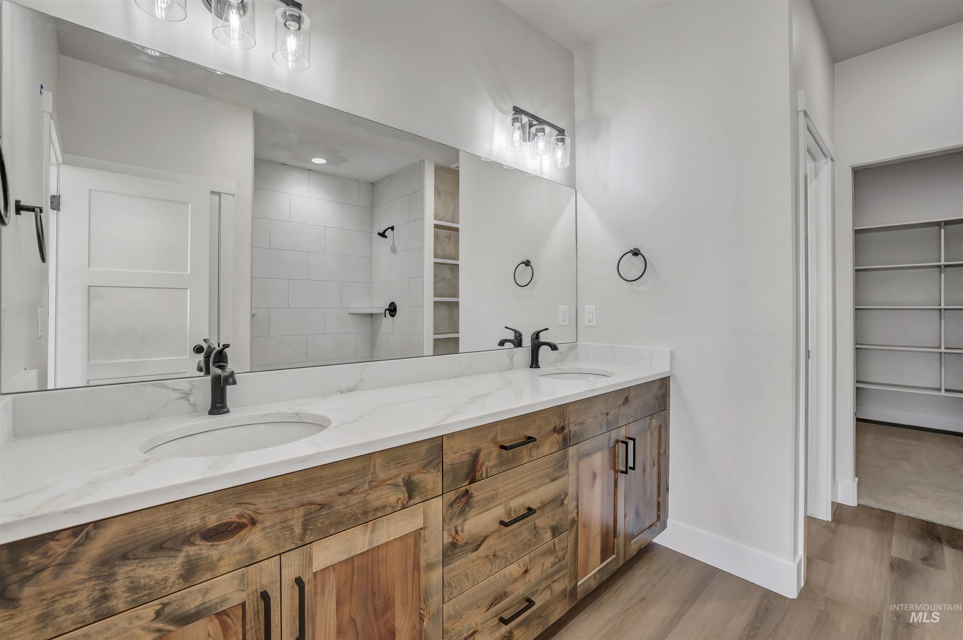 Bathroom featuring wood finished floors, double vanity, a tile shower, and a walk in closet