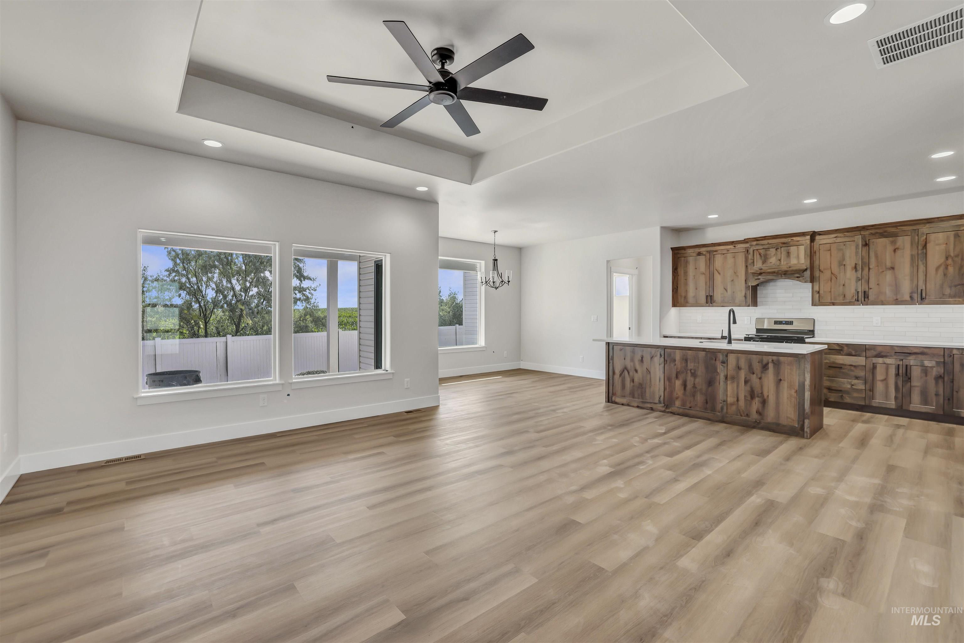 Unfurnished living room with a raised ceiling, recessed lighting, a chandelier, a ceiling fan, and light wood-style flooring
