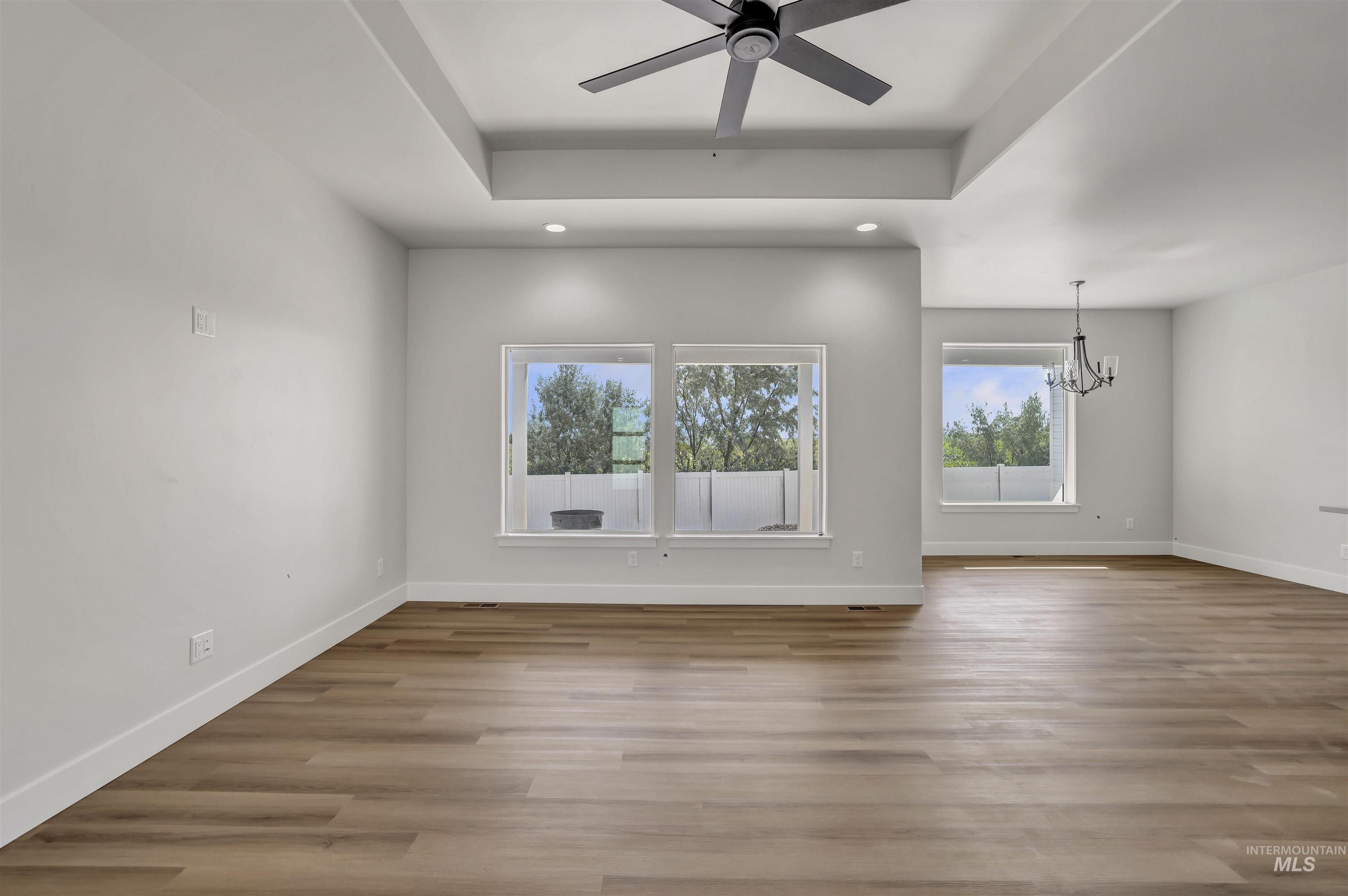 Unfurnished room with a chandelier, a ceiling fan, wood finished floors, recessed lighting, and a raised ceiling