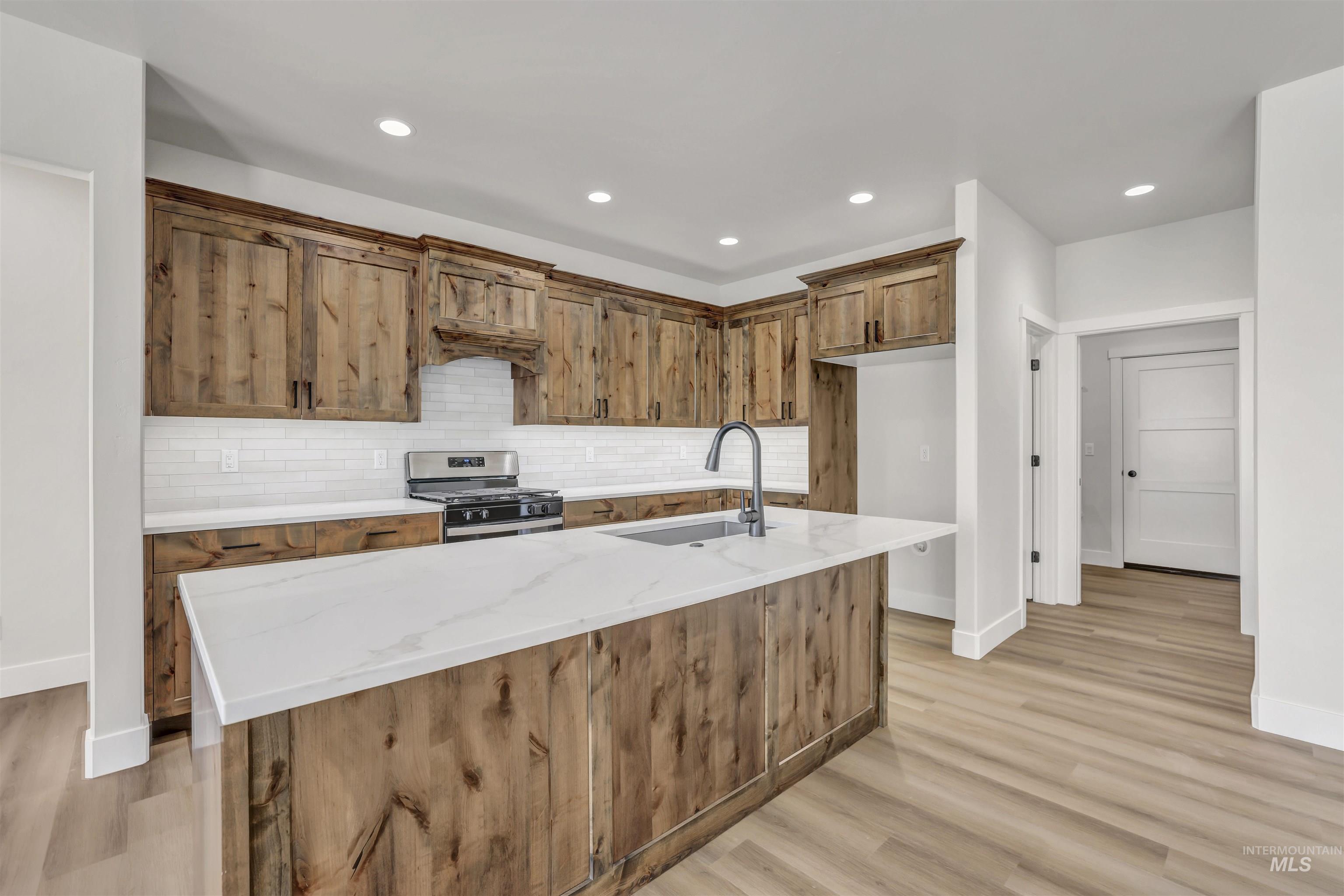Kitchen featuring stainless steel gas range oven, tasteful backsplash, light wood-style flooring, a kitchen island with sink, and recessed lighting