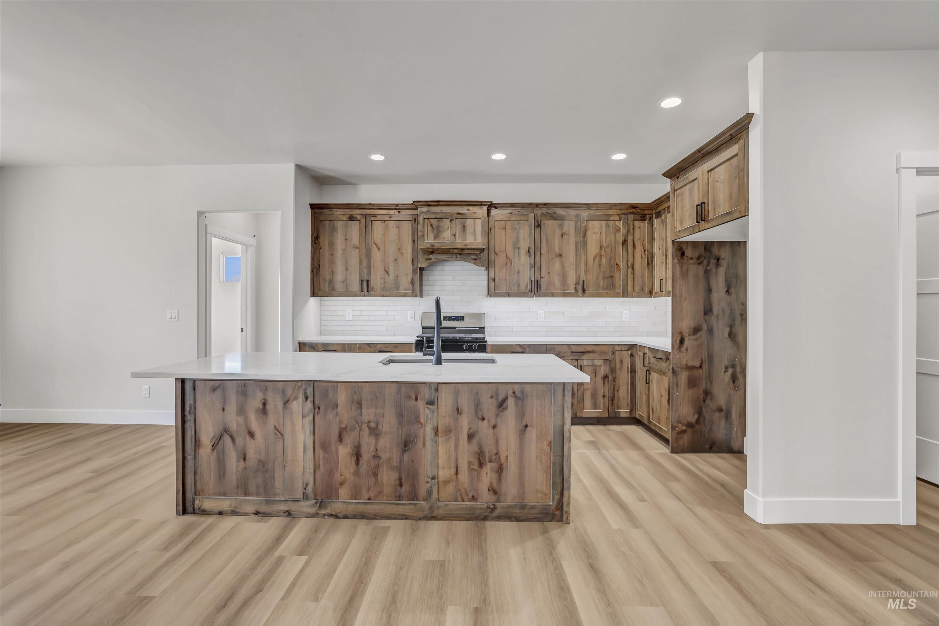 Kitchen featuring light wood finished floors, light countertops, tasteful backsplash, a kitchen island with sink, and recessed lighting