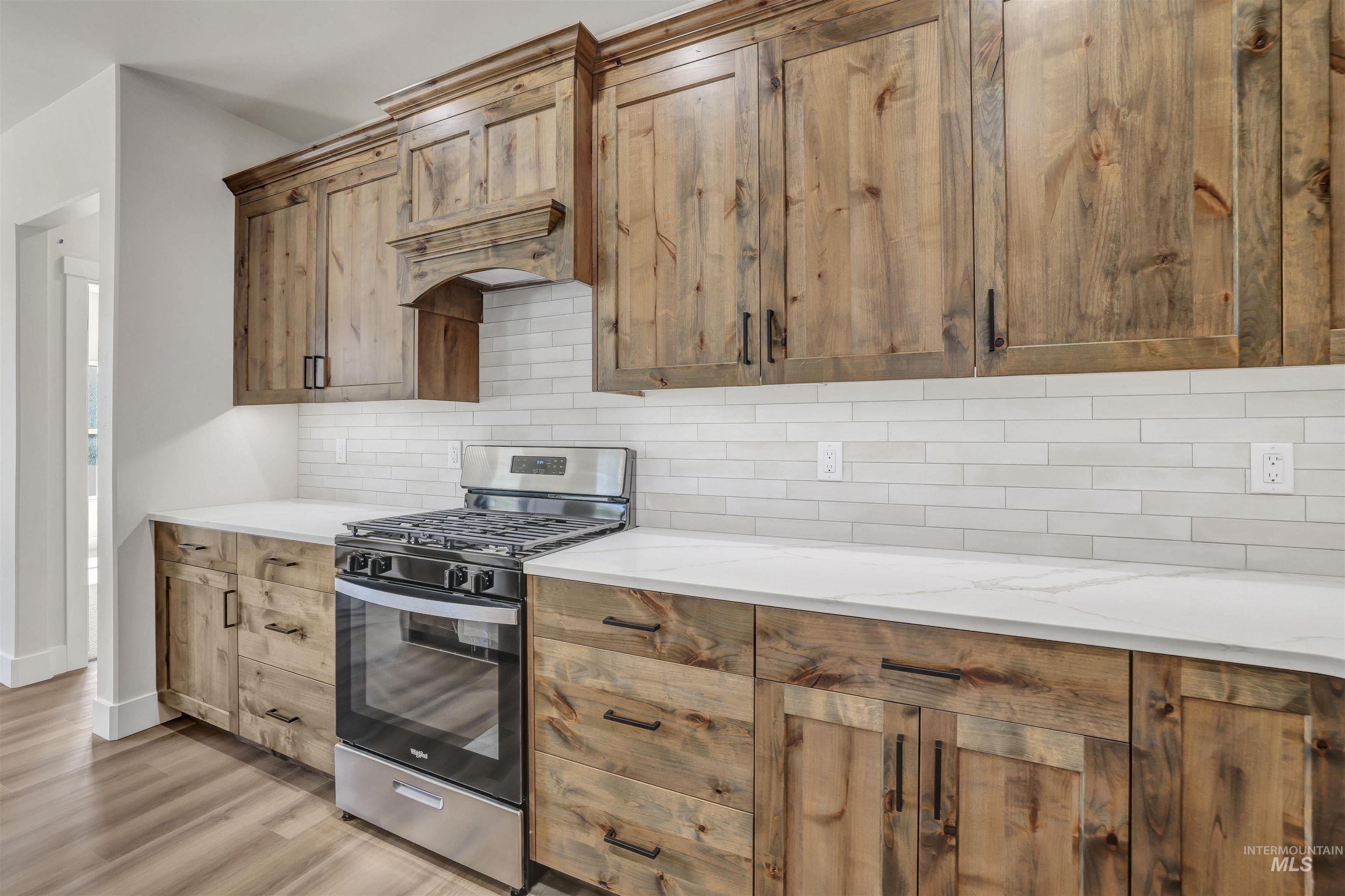 Kitchen with stainless steel gas stove, tasteful backsplash, light wood-style flooring, light stone counters, and custom range hood
