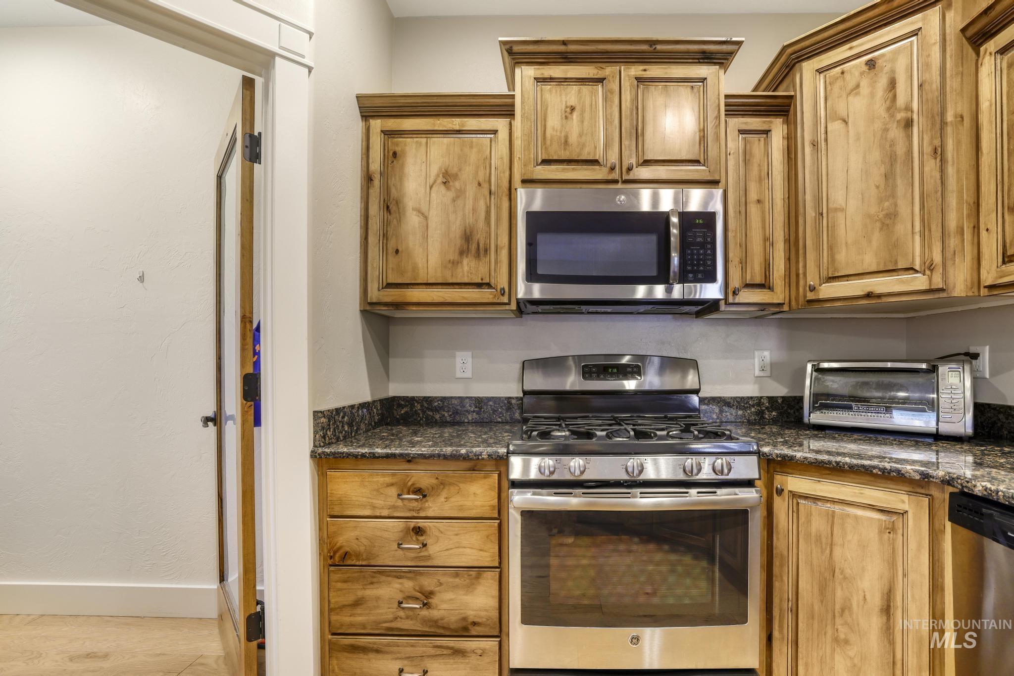 Kitchen featuring stainless steel appliances, dark stone counters, and brown cabinets