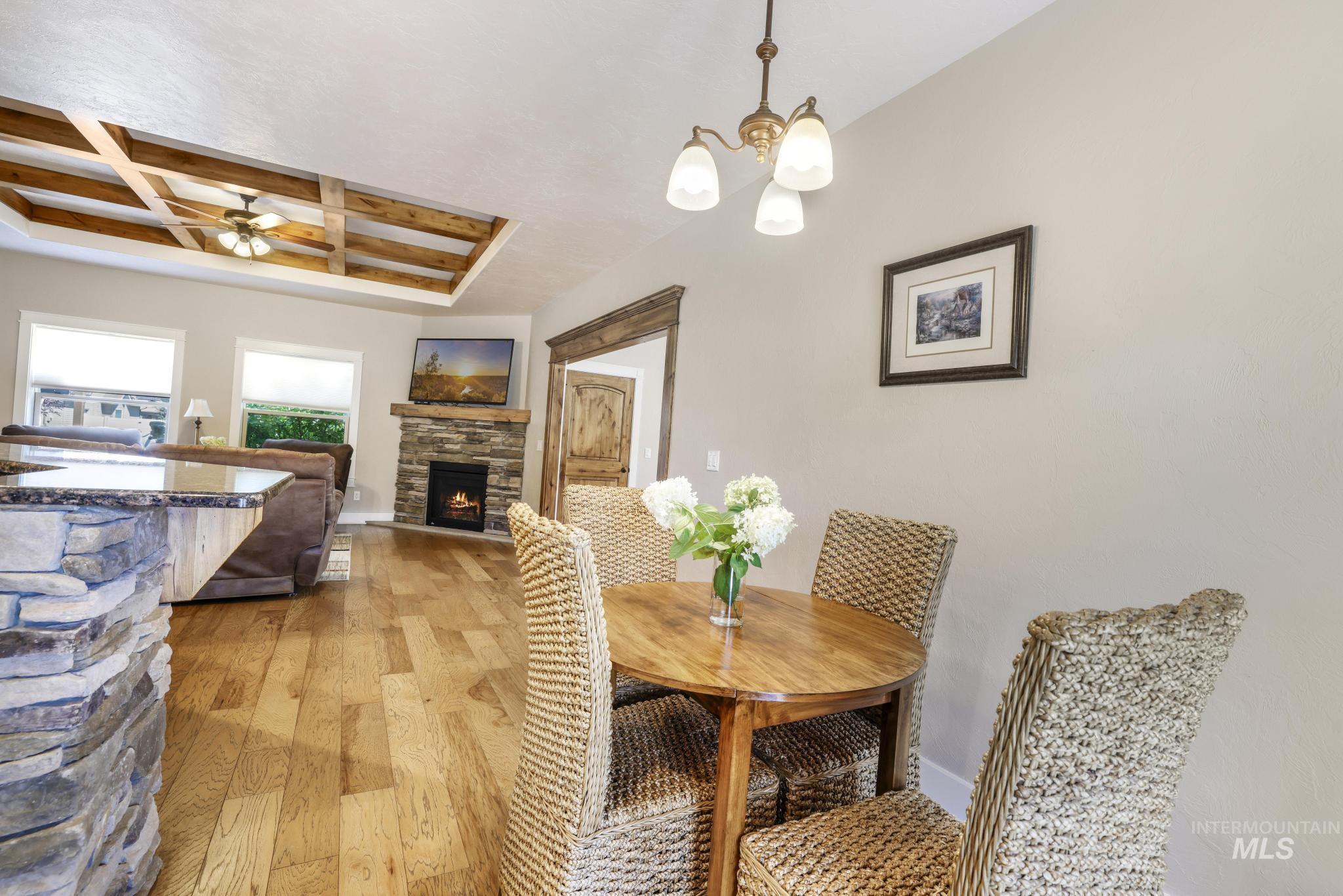 Dining space featuring light wood-style floors, coffered ceiling, a stone fireplace, beam ceiling, and a ceiling fan