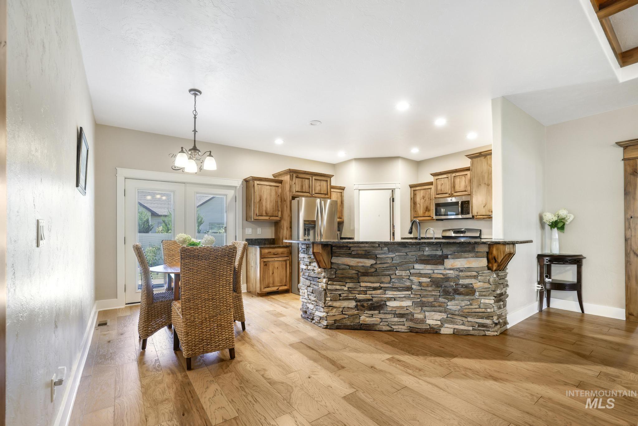 Kitchen with light wood finished floors, brown cabinetry, a peninsula, a chandelier, and pendant lighting