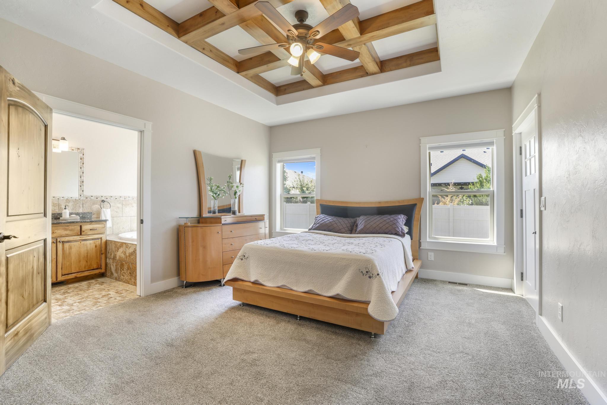 Bedroom with coffered ceiling, beam ceiling, light carpet, ceiling fan, and ensuite bathroom