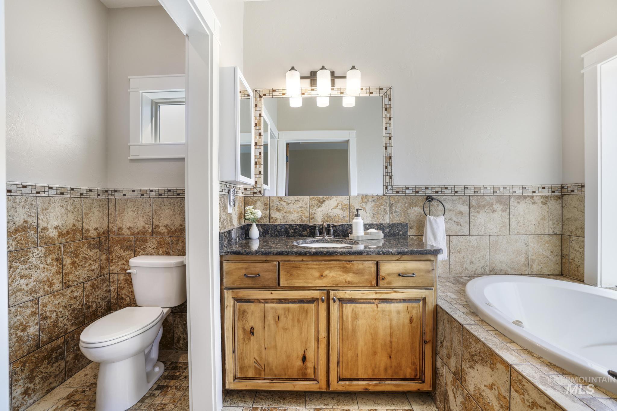 Bathroom with tile walls, vanity, a bath, and wainscoting