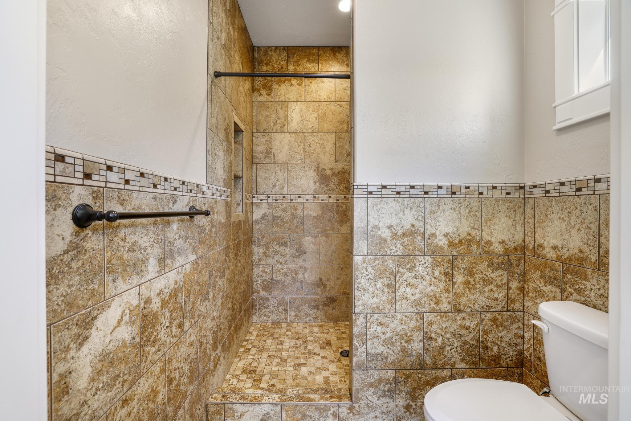 Full bathroom with a stall shower, tile walls, and a wainscoted wall